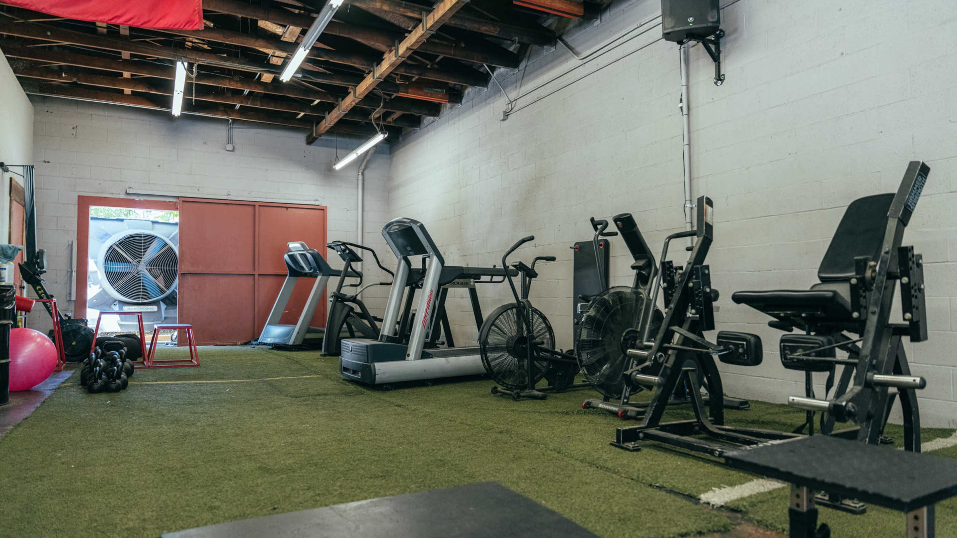 A spacious gym with exercise equipment, including treadmills, a stationary bike, and weight machines, set on green turf flooring.