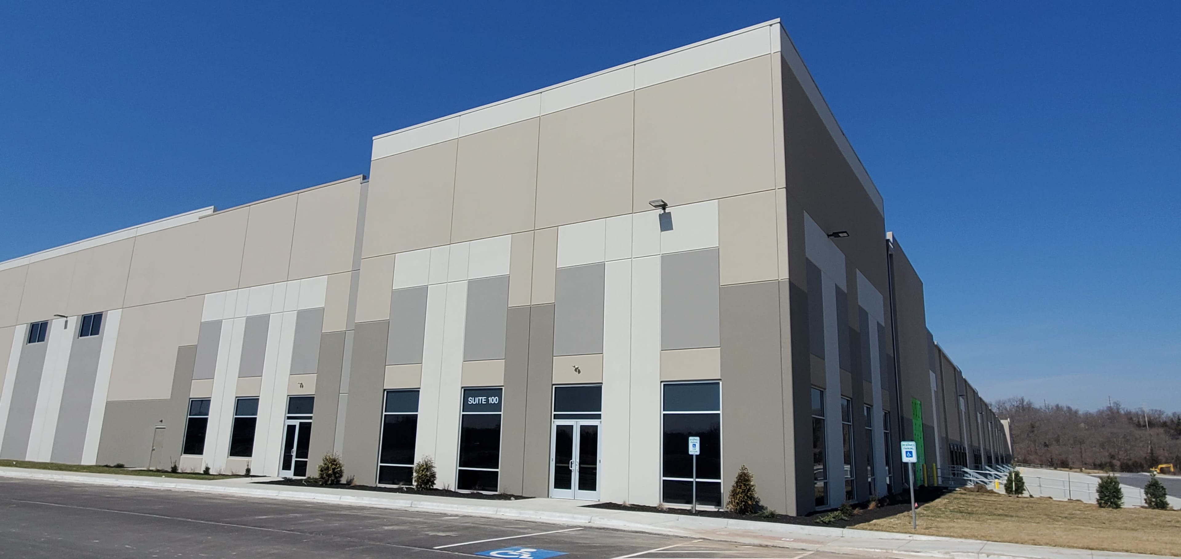 The image shows a large, modern warehouse building with a light-colored exterior under a clear blue sky.