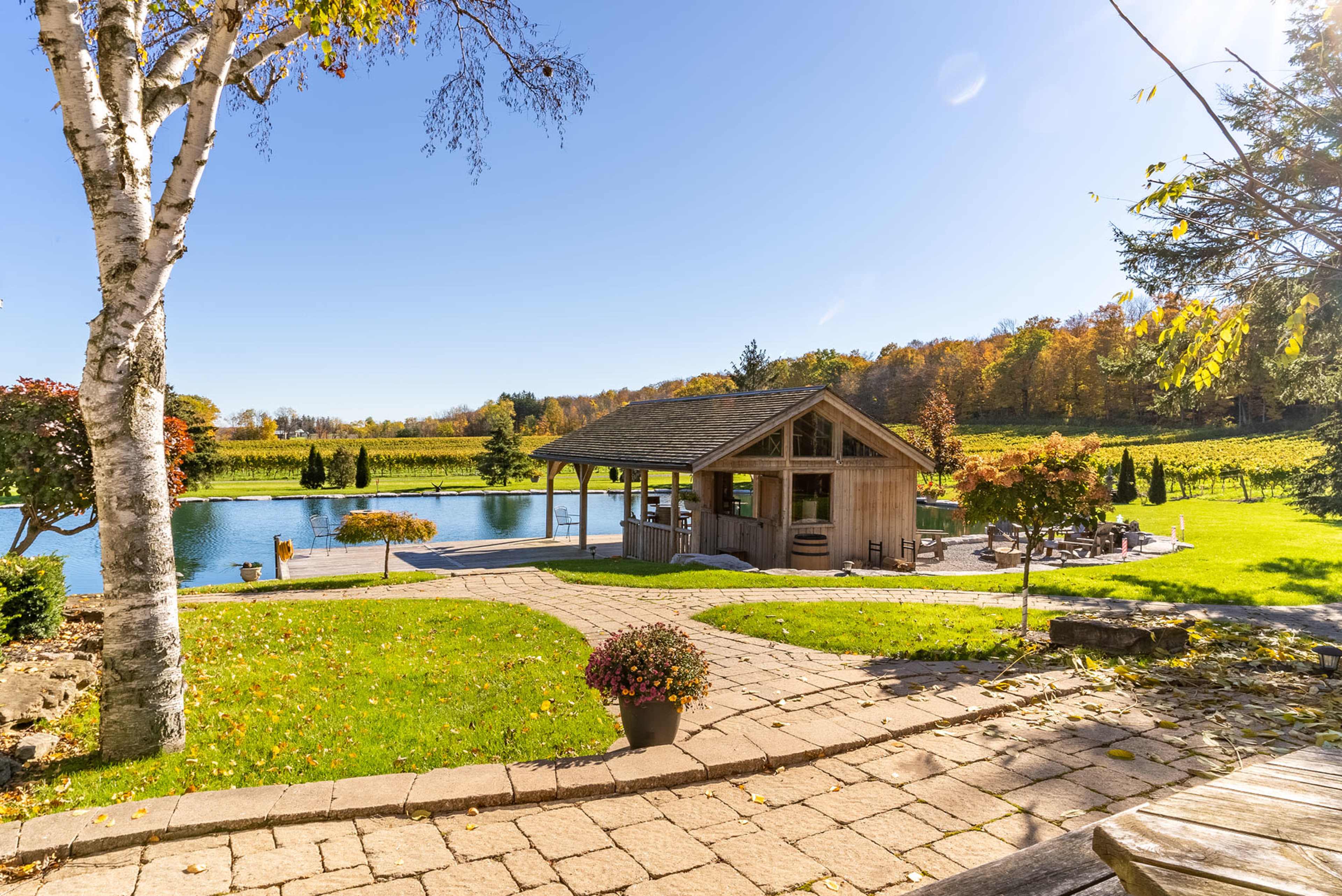 A wooden pavilion sits beside a pond surrounded by manicured lawns and trees with autumn foliage.