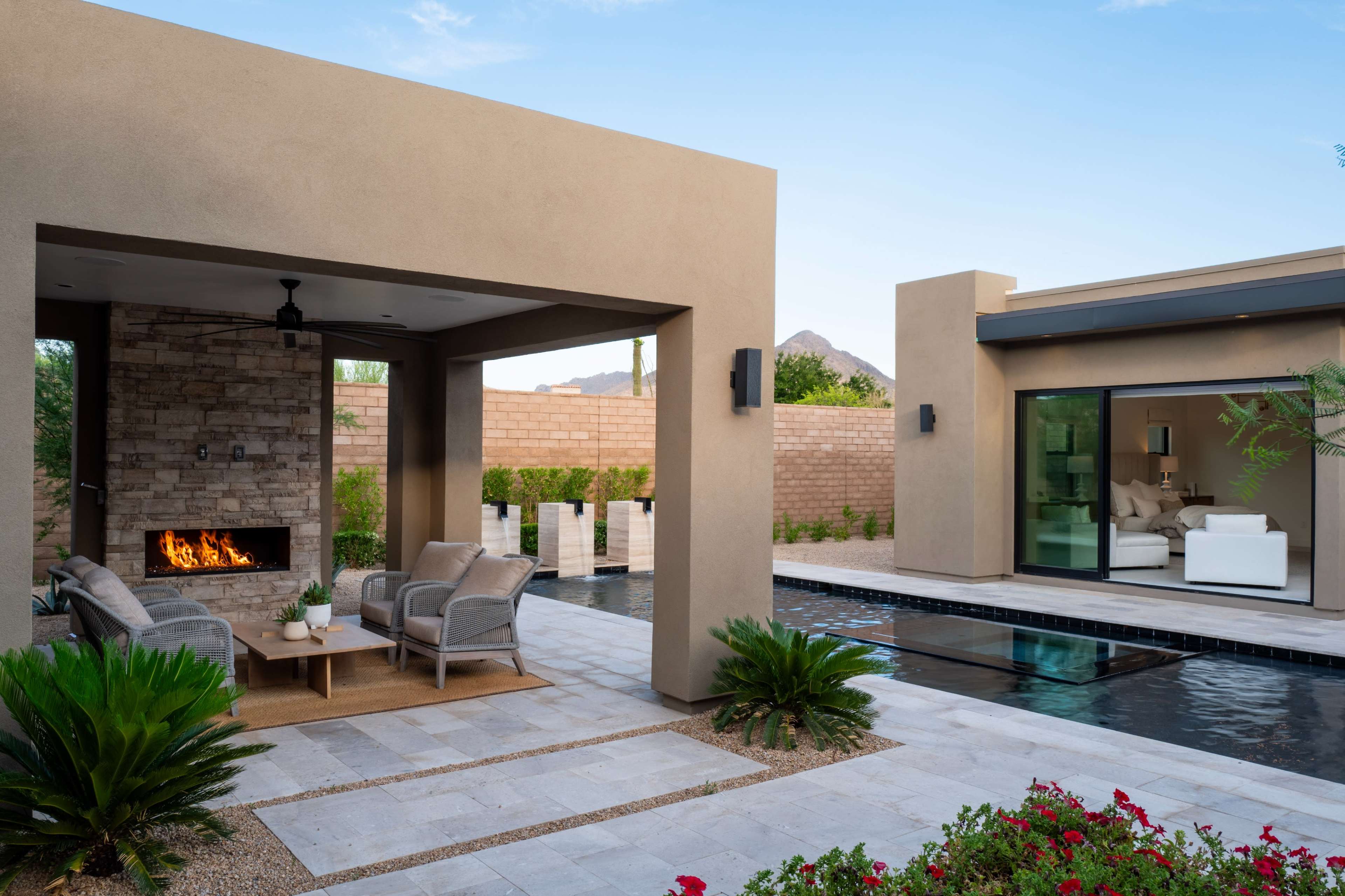 The image shows a contemporary outdoor living space with a seating area, a shallow pool, and landscaped gardens.