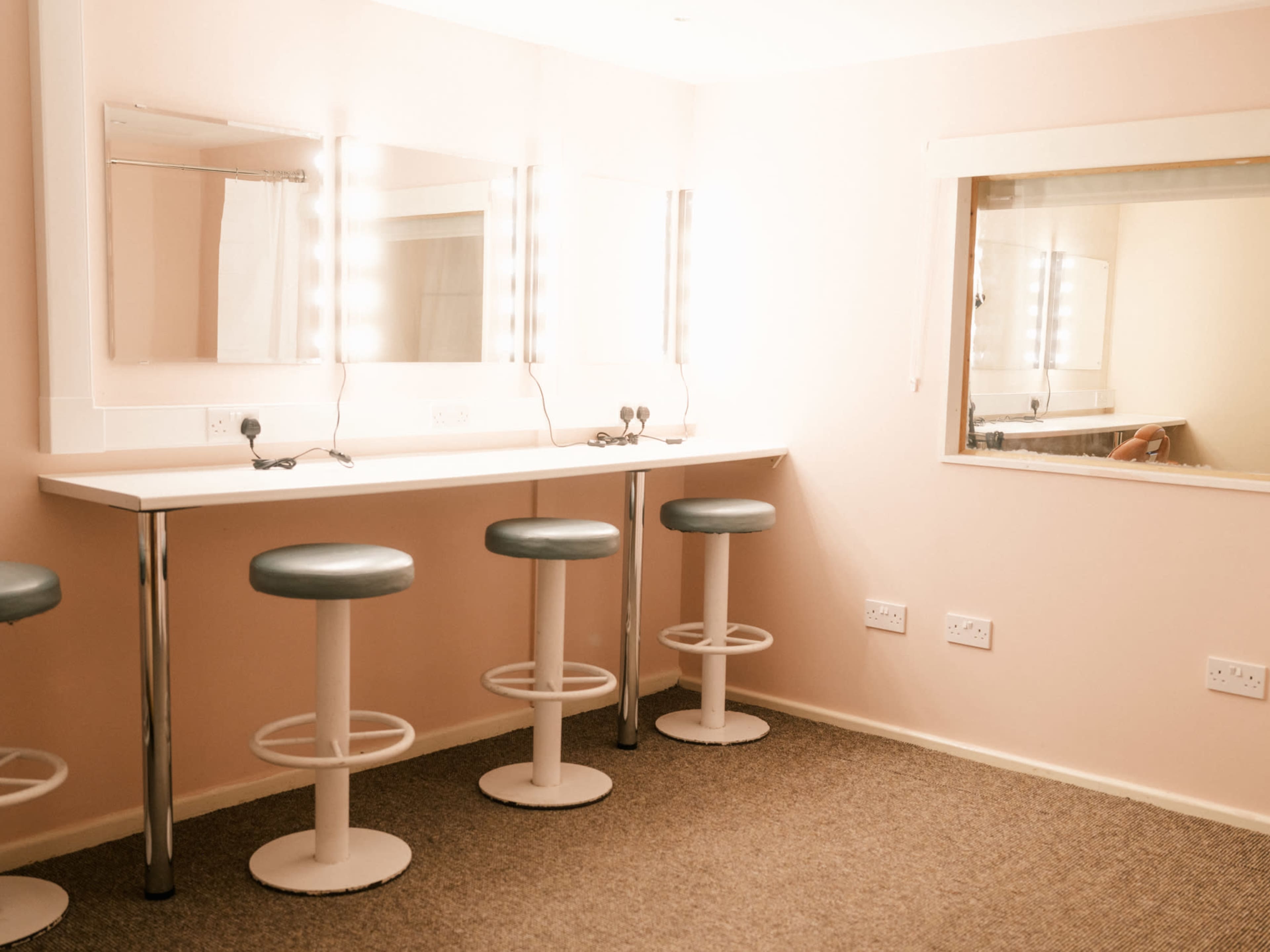 The image shows a brightly lit dressing room with a row of three stools in front of long mirrors.