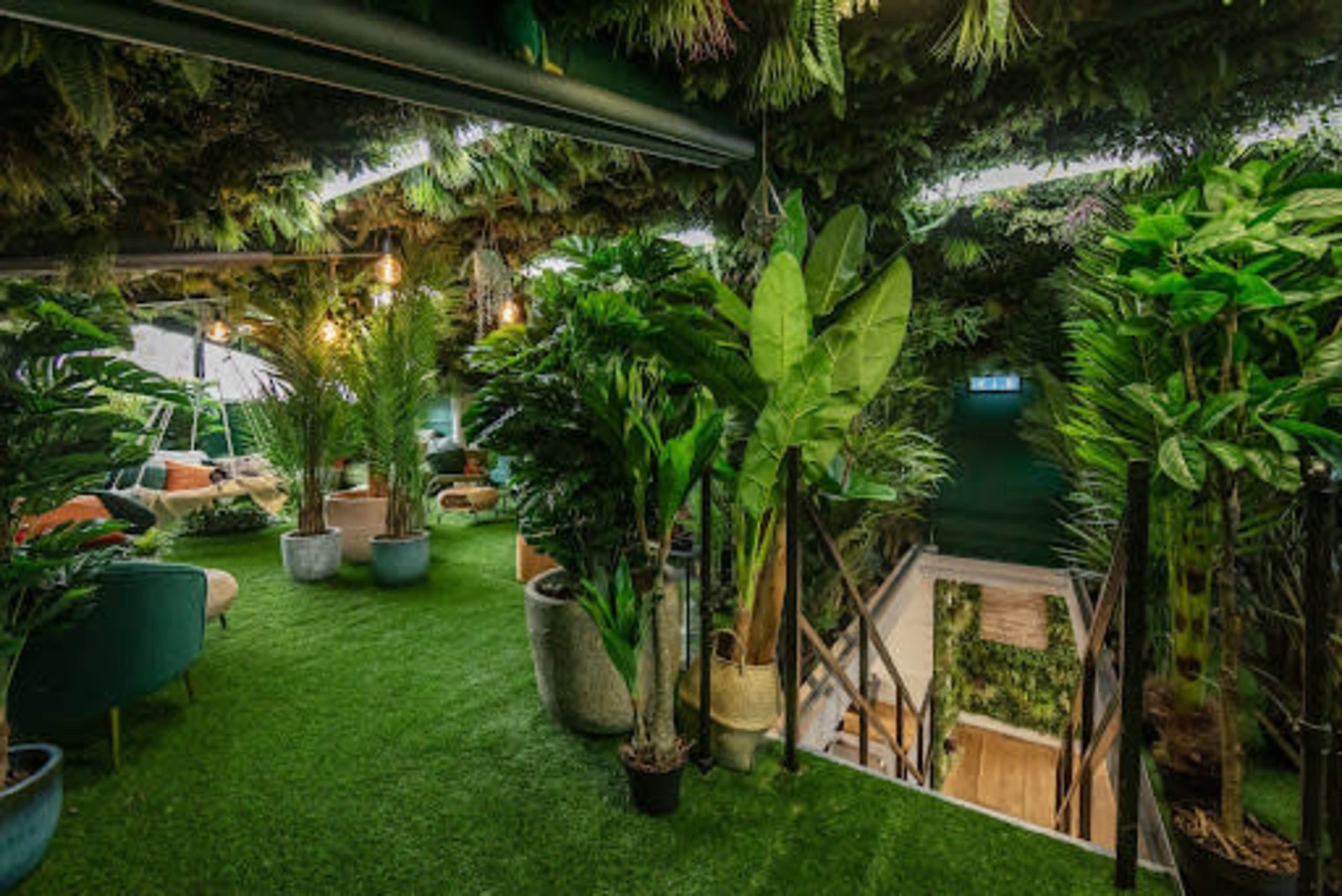 The scene shows a lush indoor space filled with various potted plants, artificial grass, and a staircase leading to a lower level.