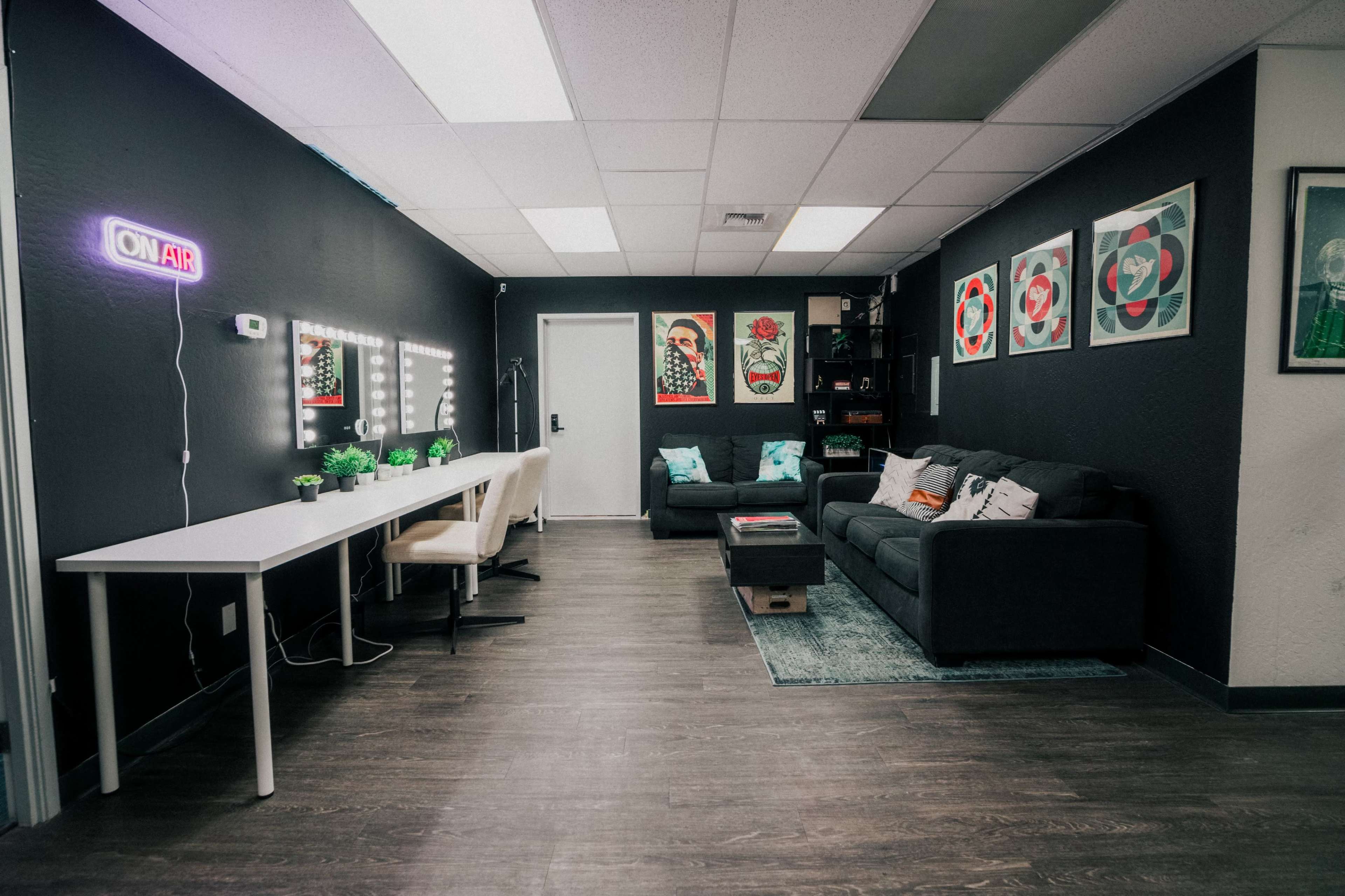 A modern workspace with a gray couch, a white table with chairs, wall art, and a "ON AIR" sign in a well-lit room.