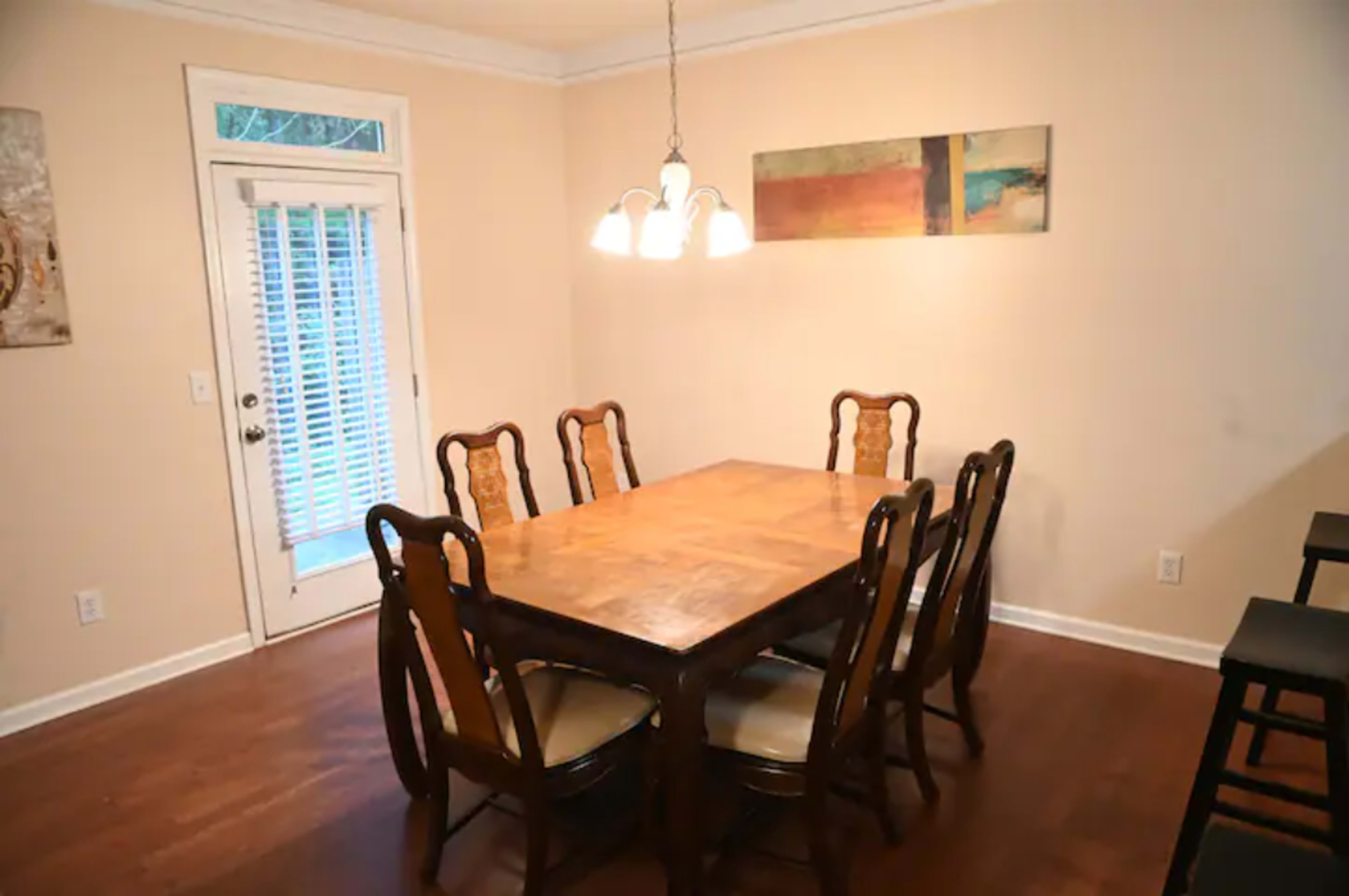 A dining room features a large wooden table surrounded by eight chairs and a sliding glass door opening to the outside.