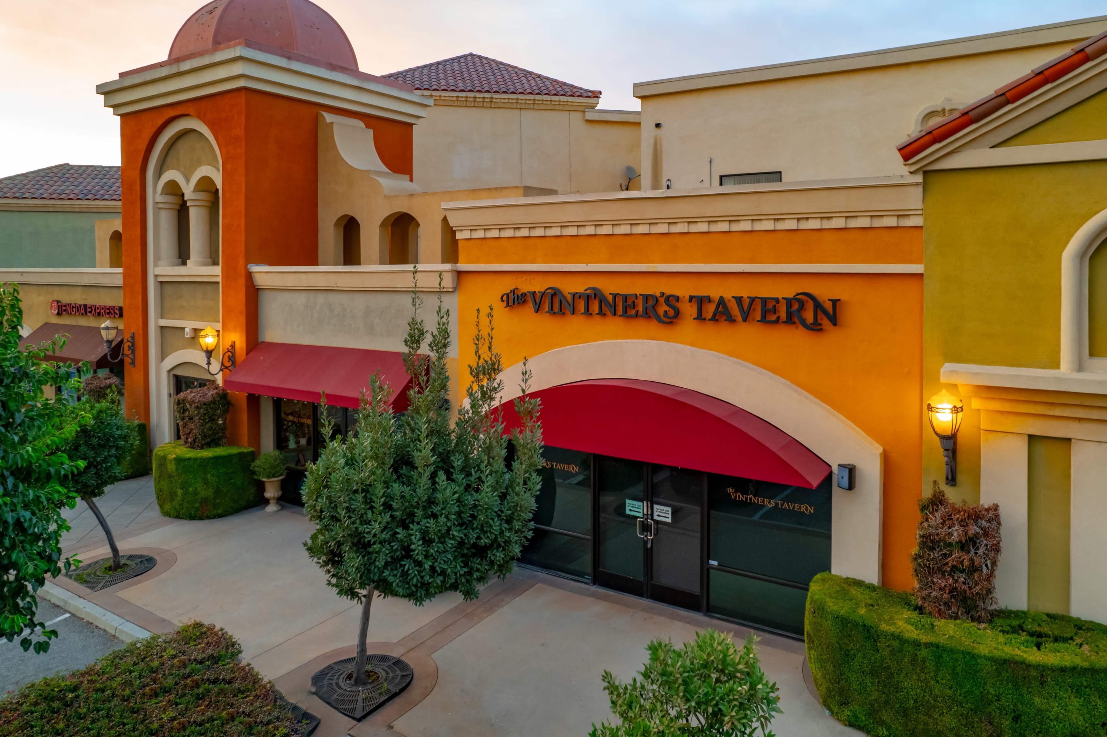 The image shows a restaurant facade with a prominent sign reading "Winthers Tavern" and a red awning, surrounded by landscaped greenery and a colorful building exterior.
