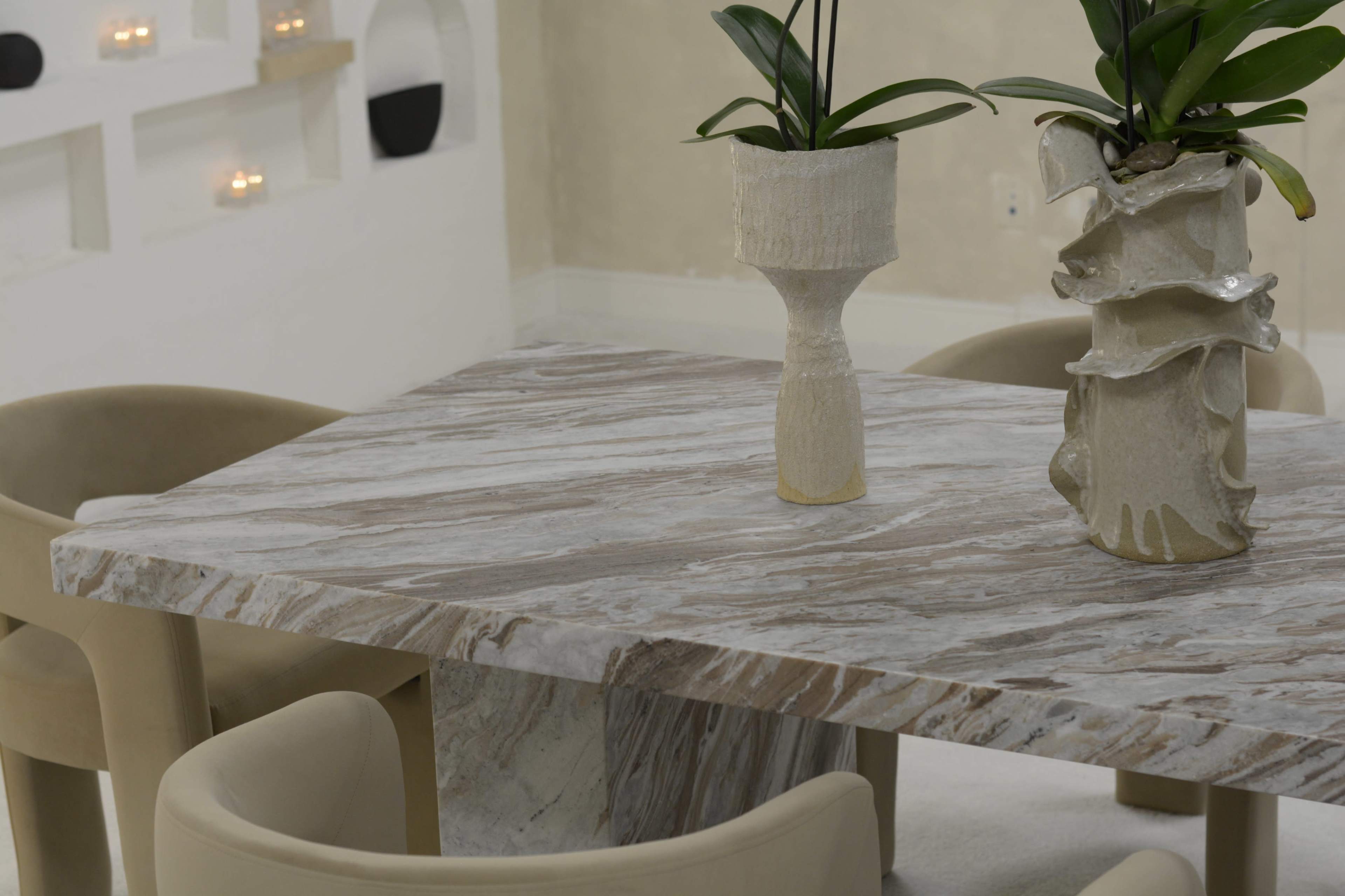 A marble table with two potted plants is situated in a room with light-colored walls and four upholstered chairs.