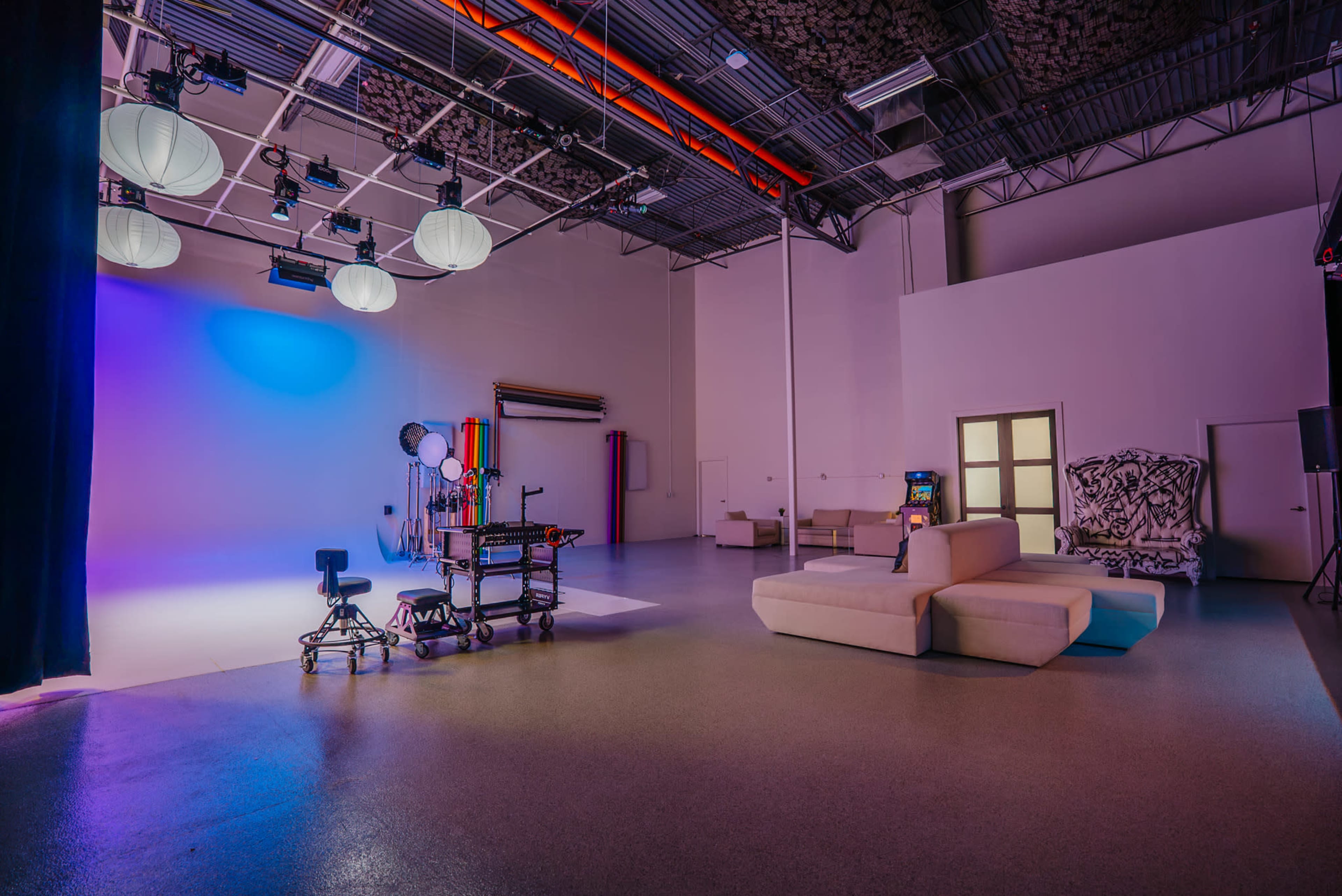 The image shows a spacious, well-lit studio with a white backdrop, equipment stands, and a white sofa arranged in the corner.