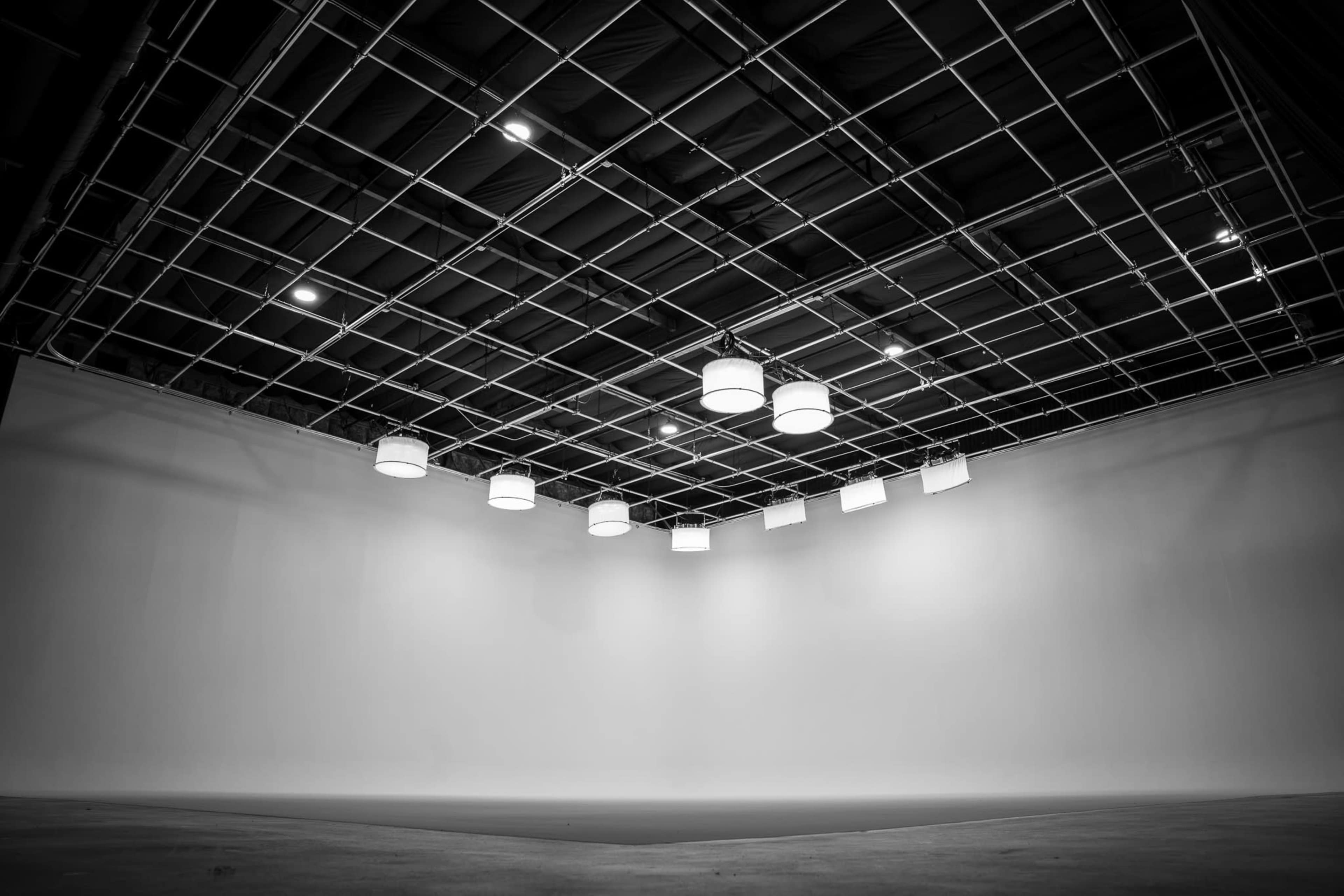 The image shows a large, empty room with a grid ceiling and multiple hanging light fixtures.