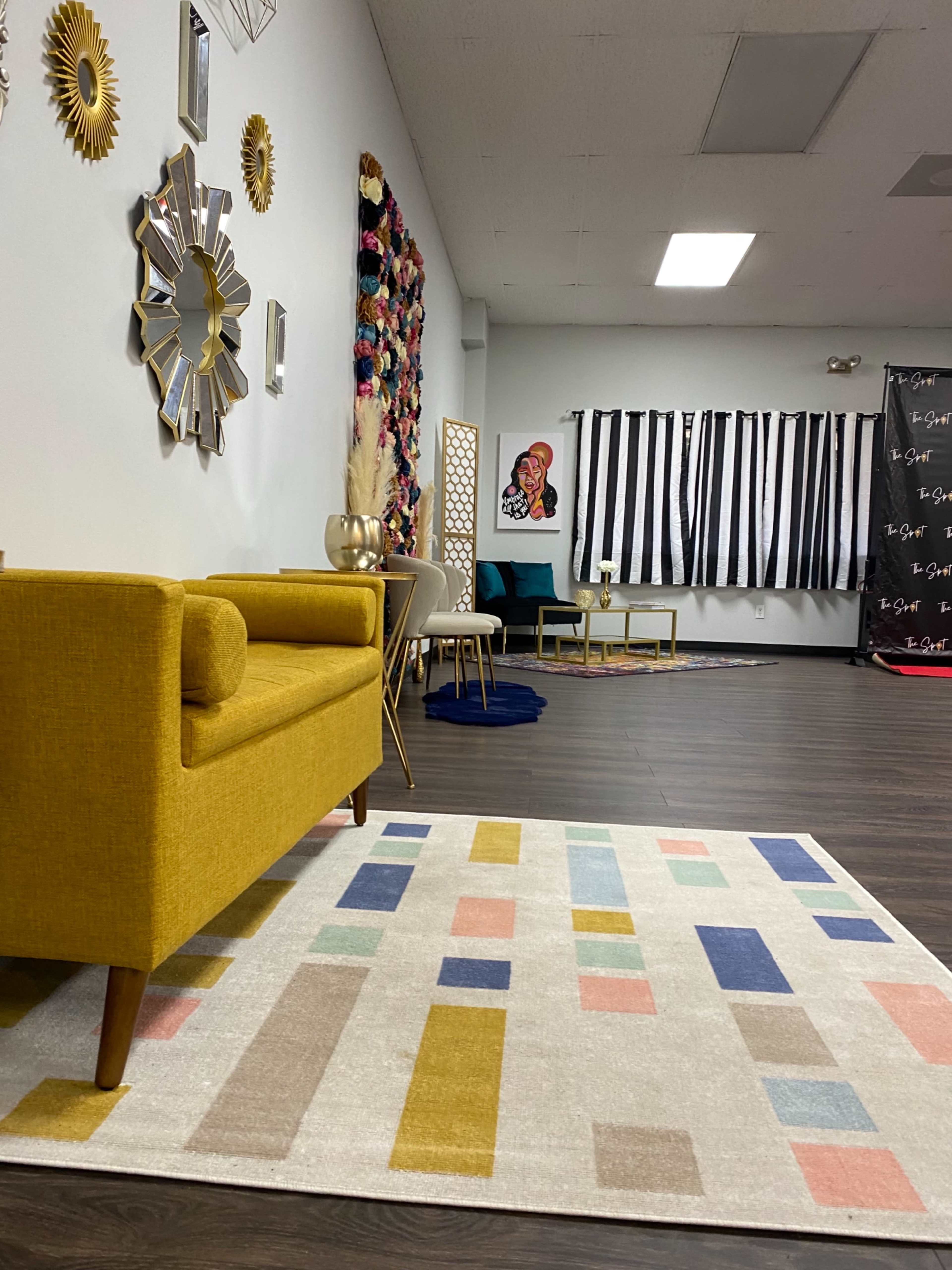 A modern interior space featuring a yellow couch, a patterned area rug, and various decorative elements on the walls, including artwork and mirrors.