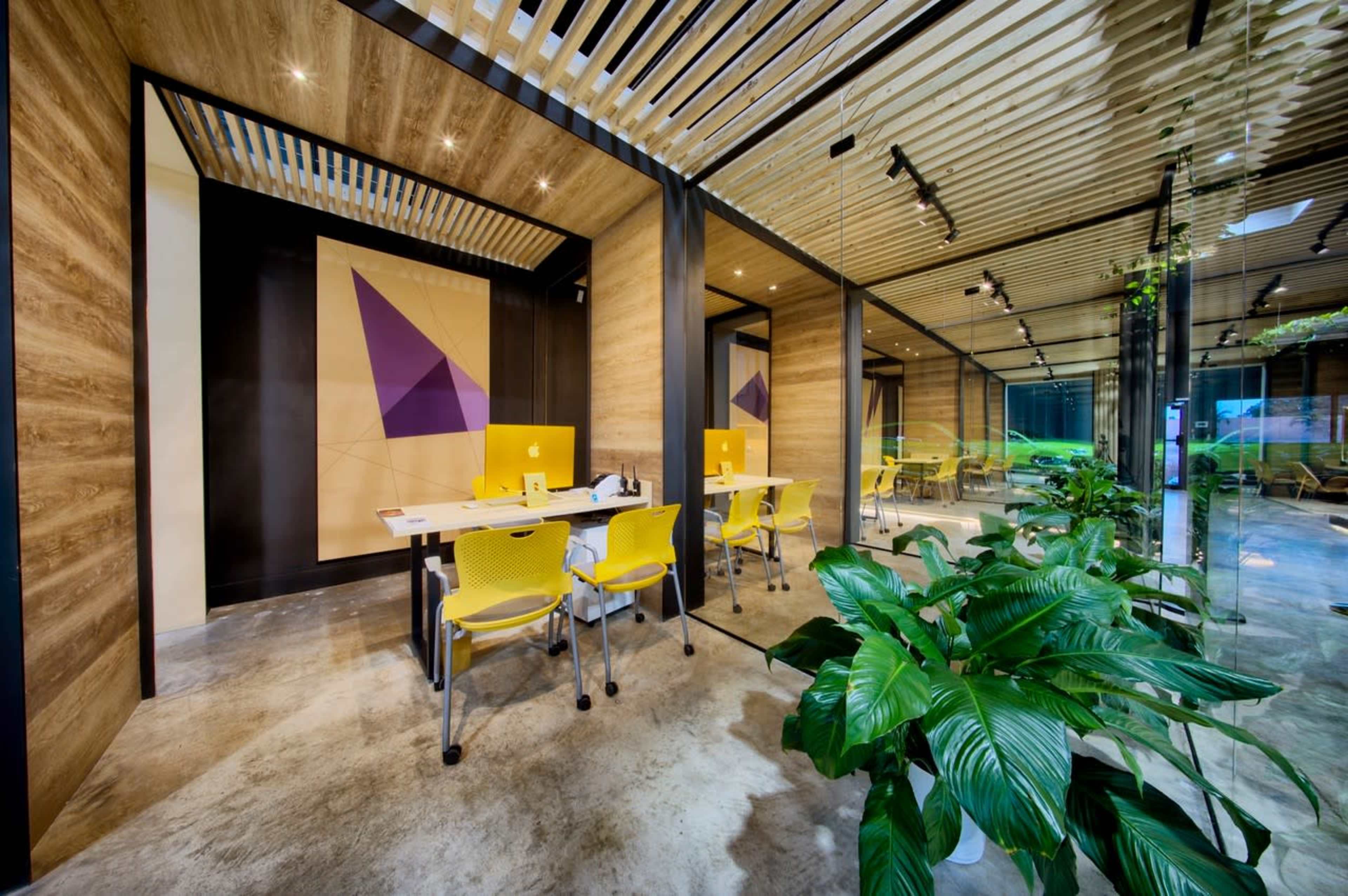A modern office space with yellow chairs, glass walls, and wooden accents, featuring geometric artwork on the wall.