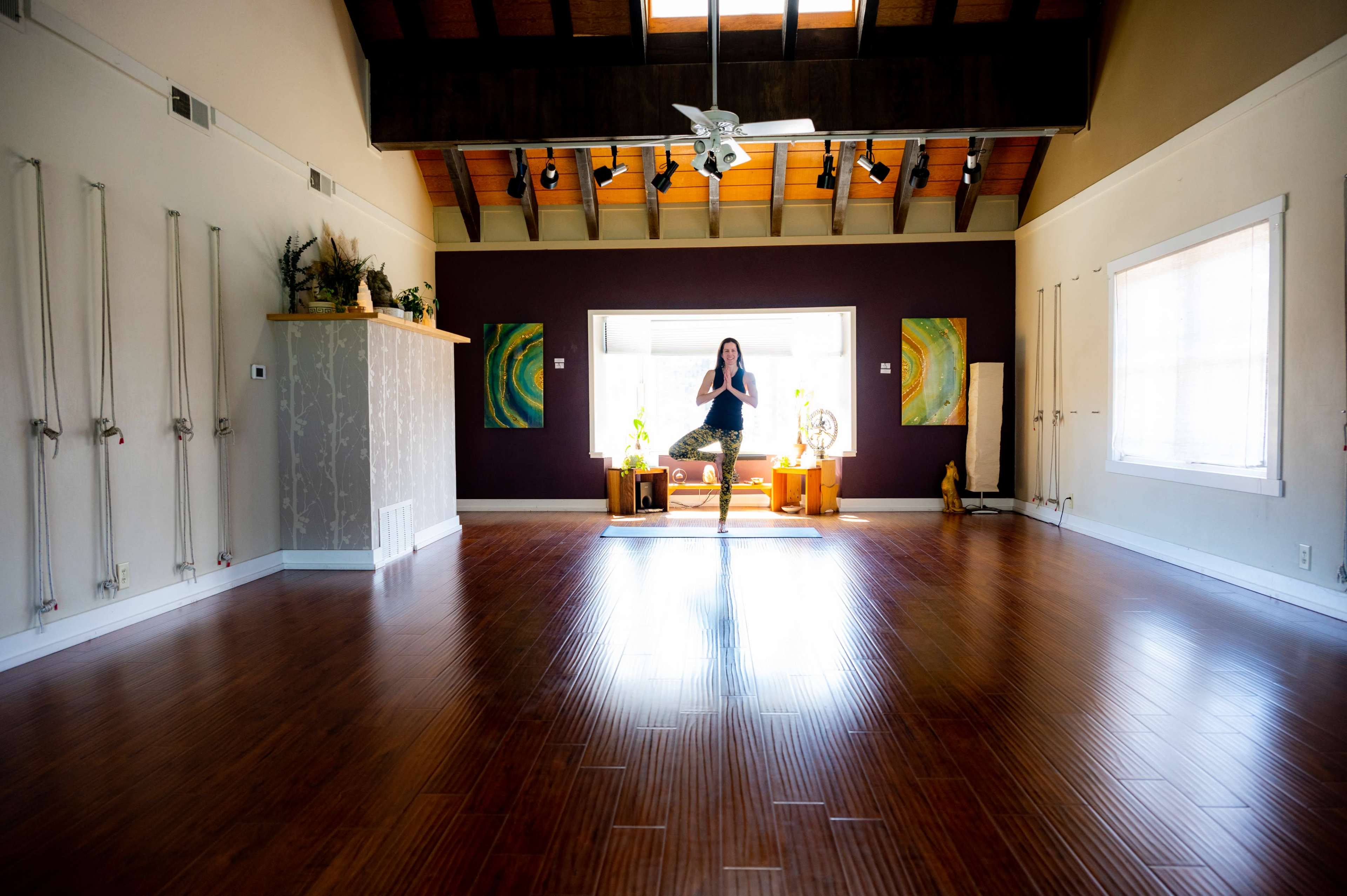 A person demonstrates a yoga pose in a spacious studio with wooden floors and calming decorations.