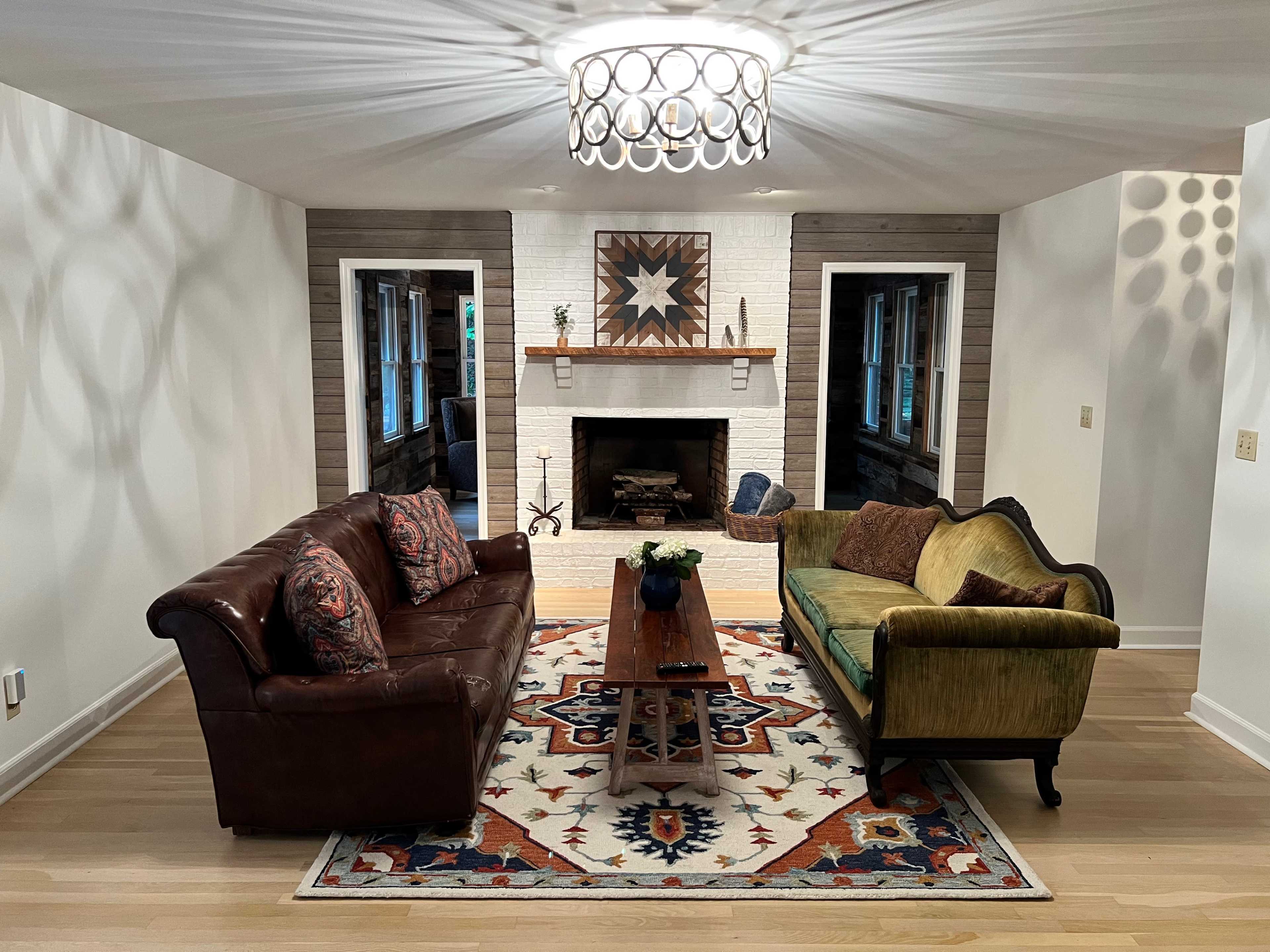 A cozy living room with two sofas, a coffee table in the center, and a fireplace surrounded by white brick.