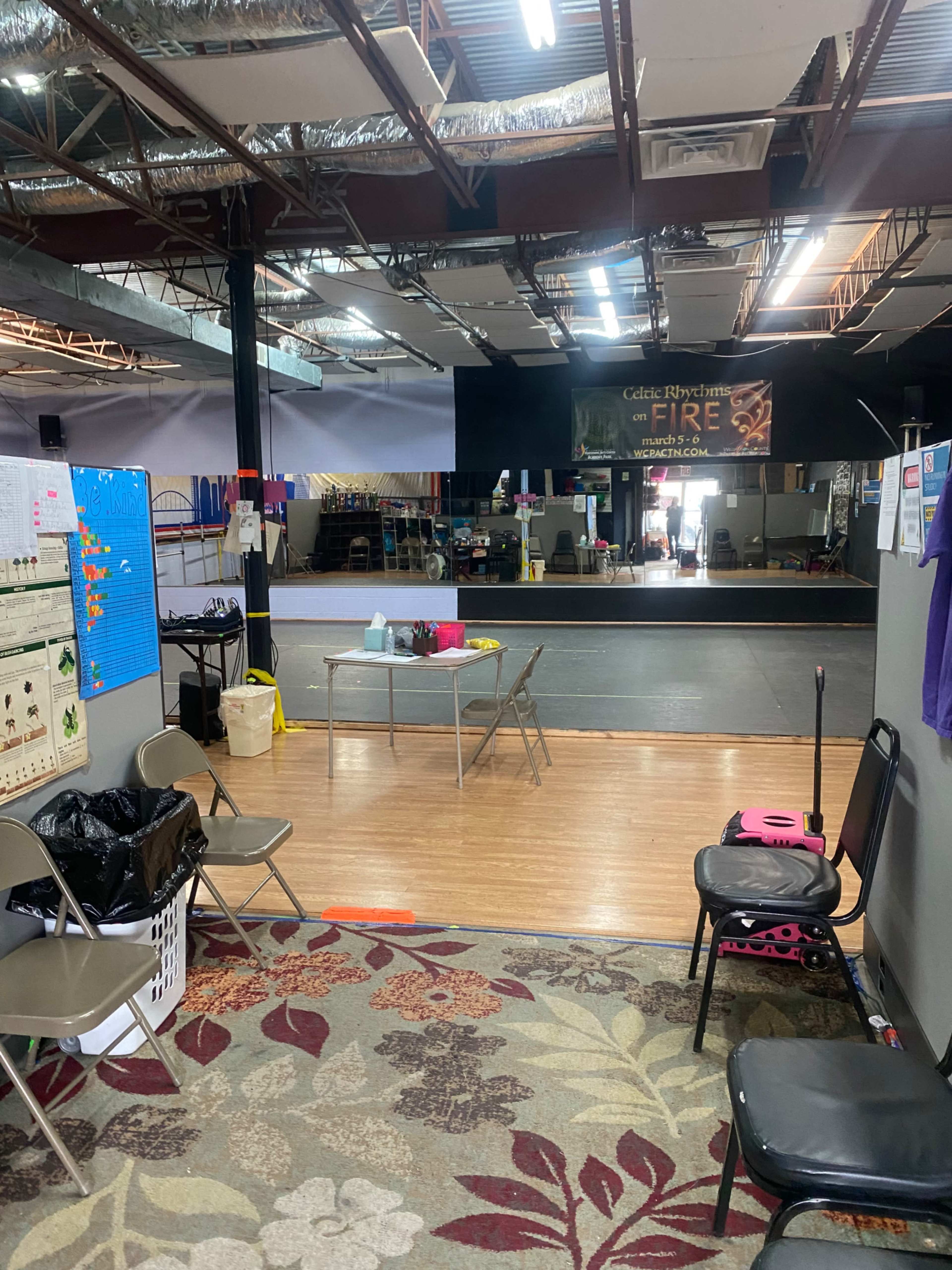 A spacious indoor recreation area with a wooden floor, various seating options, and a visible performance stage in the background.