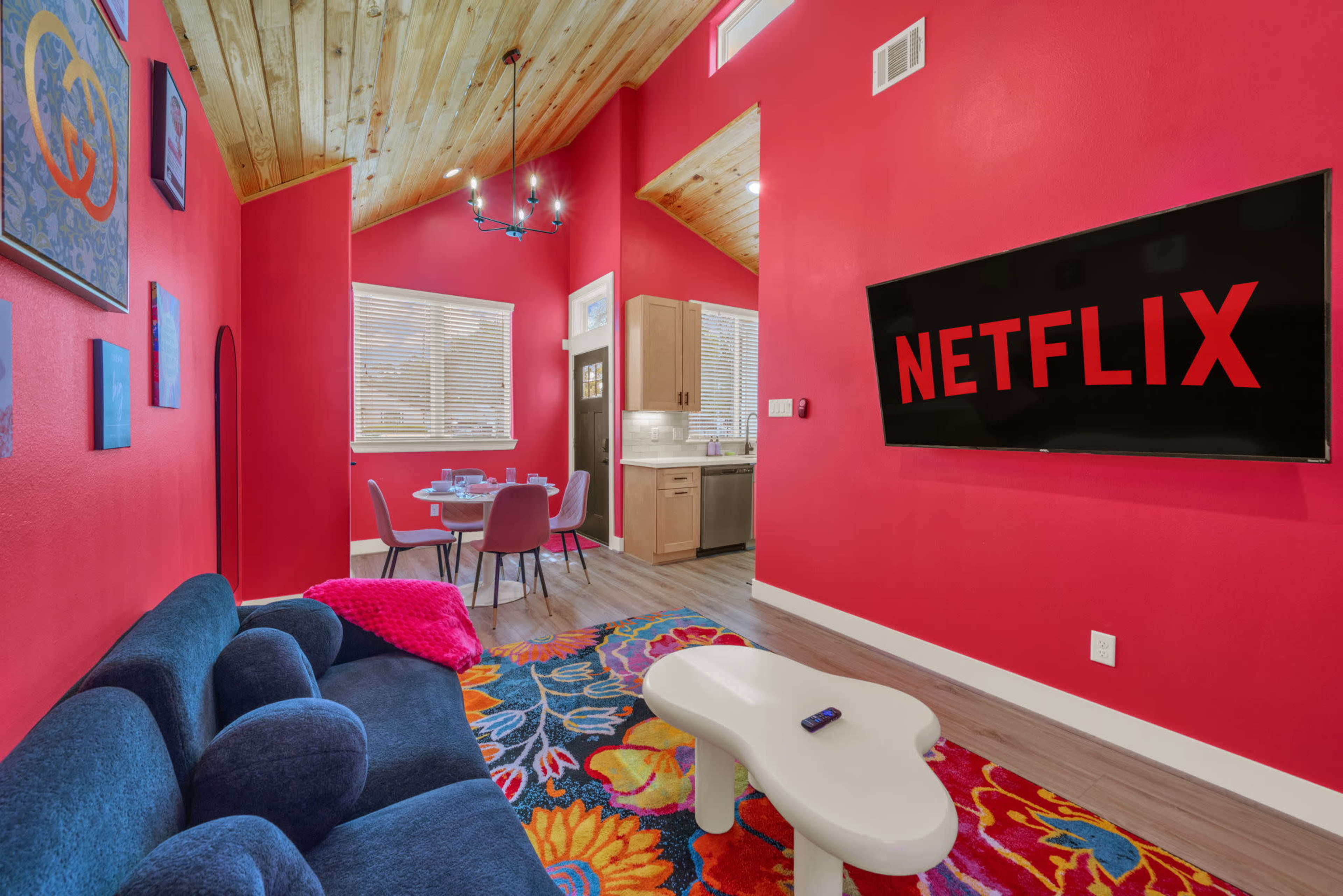 The image features a vibrant living room with a pink accent wall, a blue couch, a colorful floral rug, and a television displaying the Netflix logo.