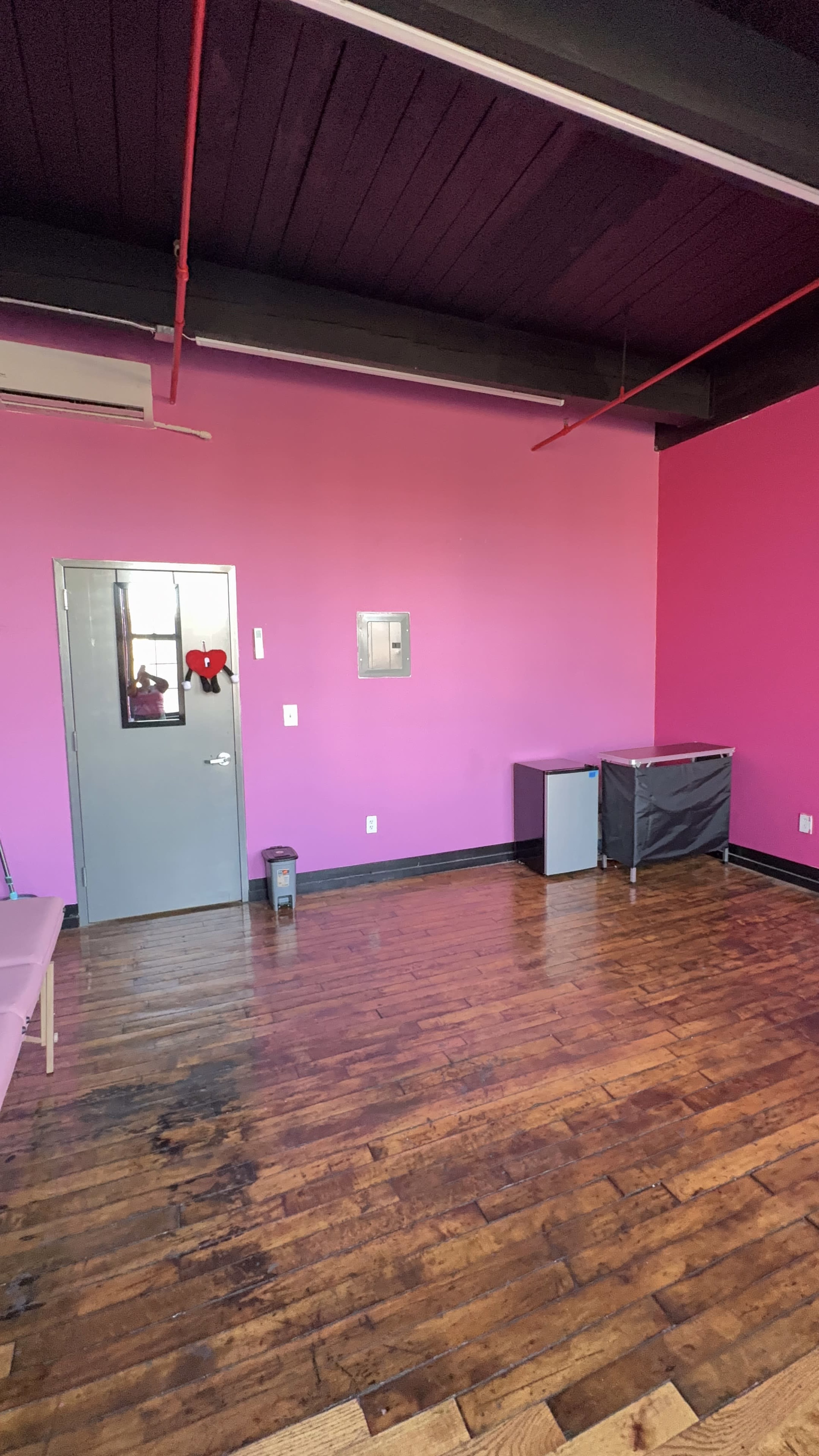 The image shows a room with pink walls, a wooden floor, a door, and a few pieces of furniture including a cabinet and a bin.