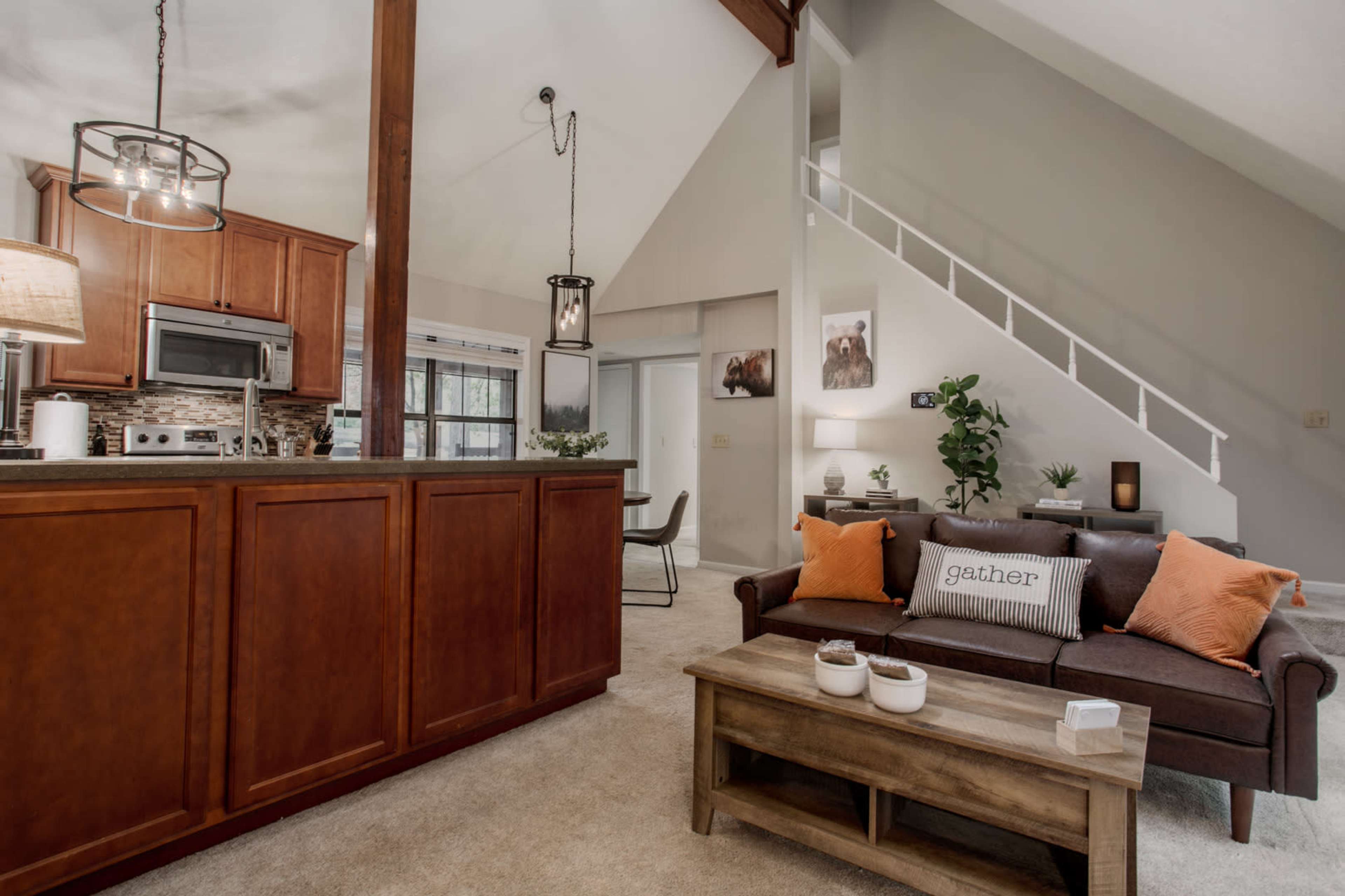 A modern living space featuring a kitchen with wooden cabinets, a brown sofa adorned with cushions, and a dining area visible in the background.