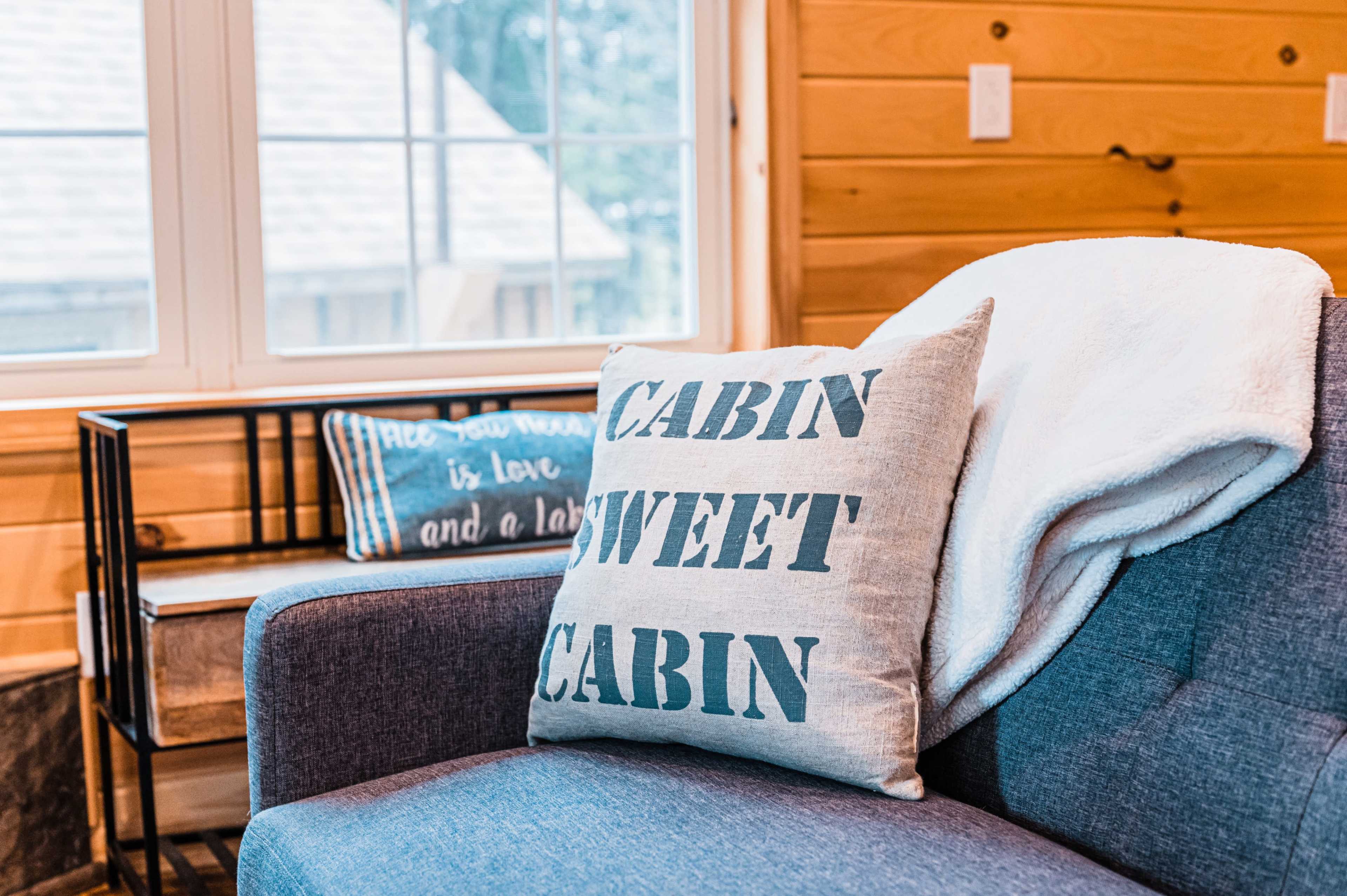 A cozy cabin interior features a gray sofa adorned with two decorative pillows and a white throw blanket.