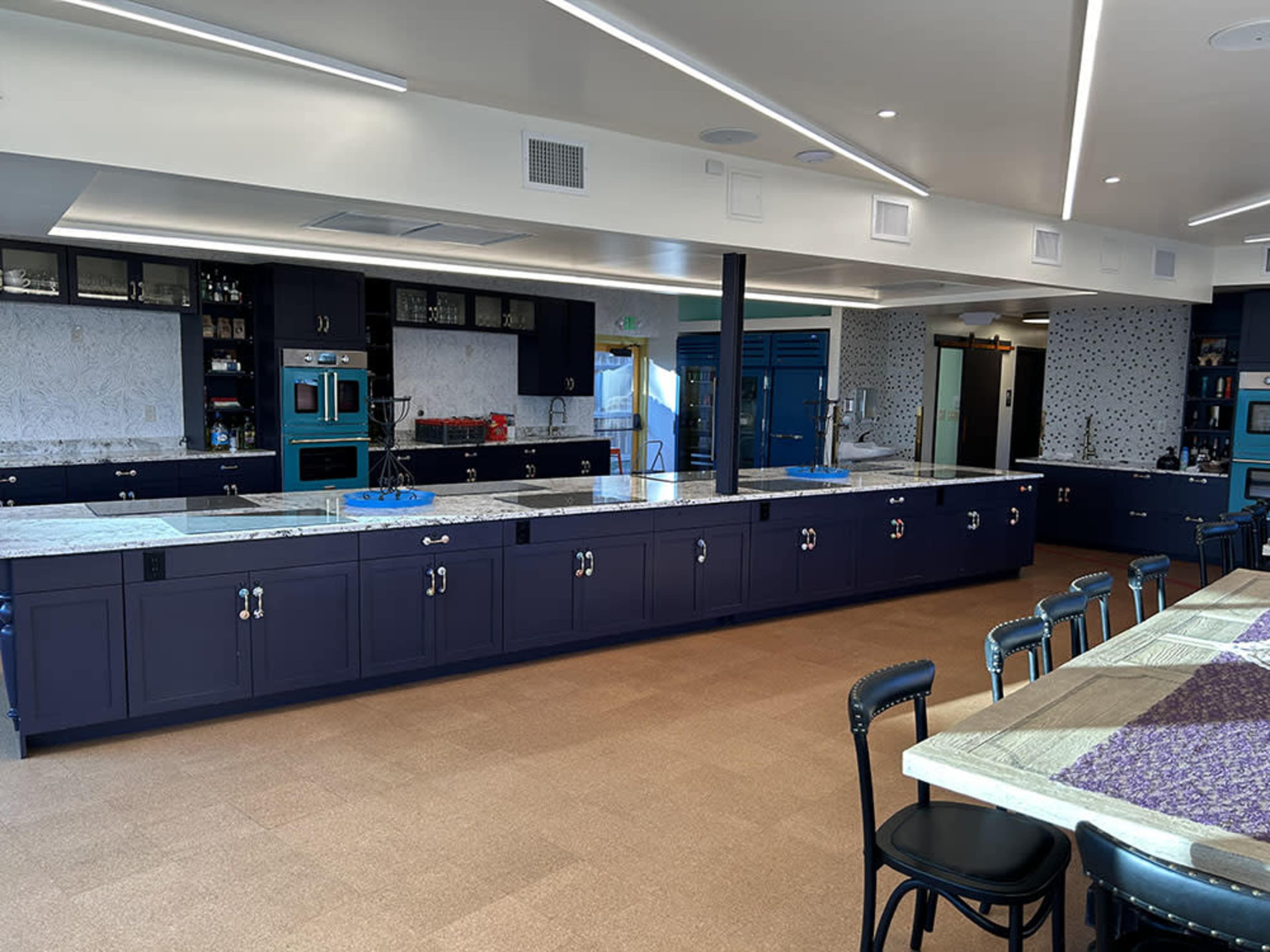 The image shows a modern kitchen featuring dark cabinetry, a large central island with a granite countertop, and a spacious dining area with black chairs.