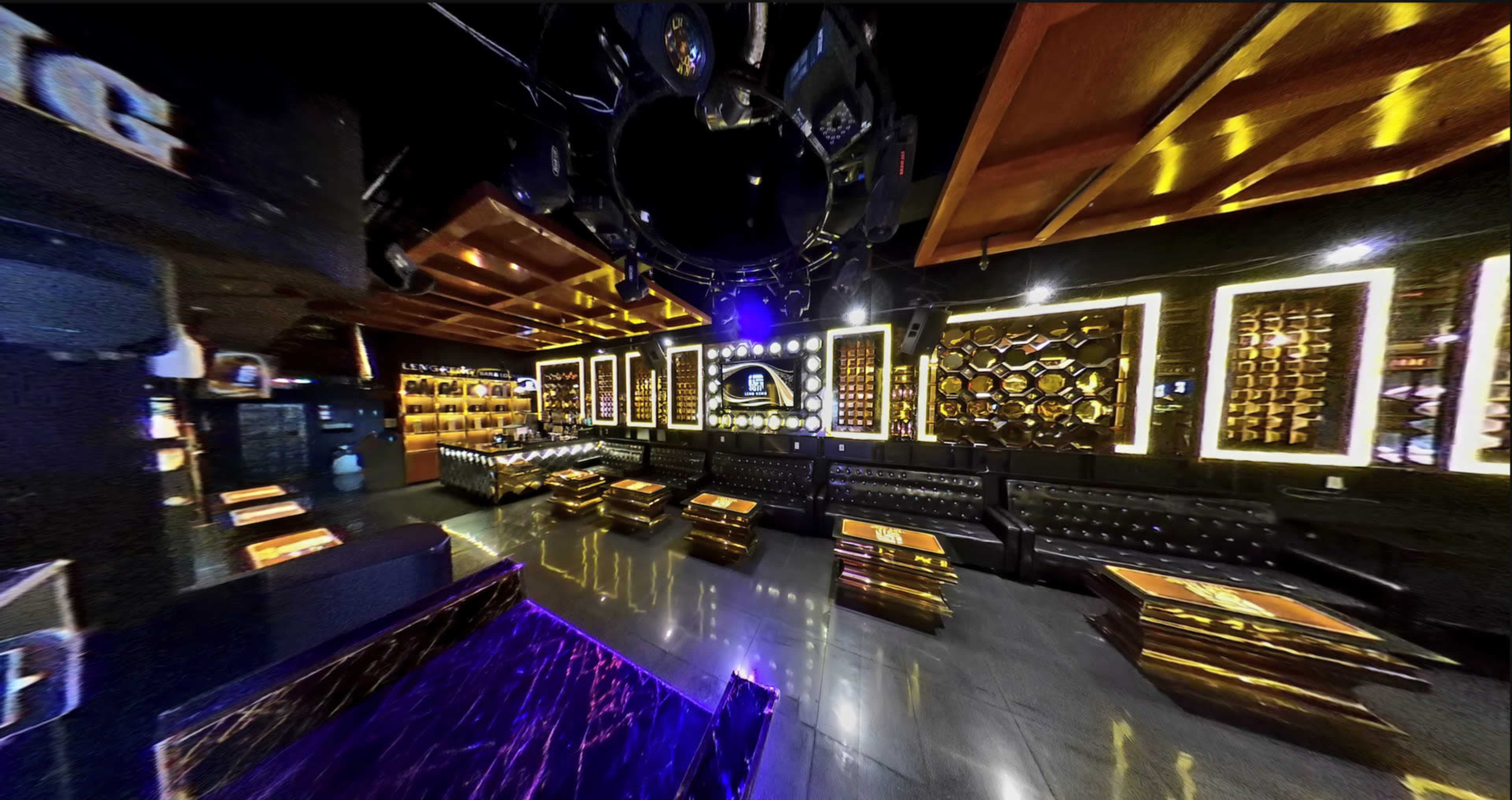 An upscale lounge with leather seating, illuminated decor, and a bar area featuring shelves of bottles.
