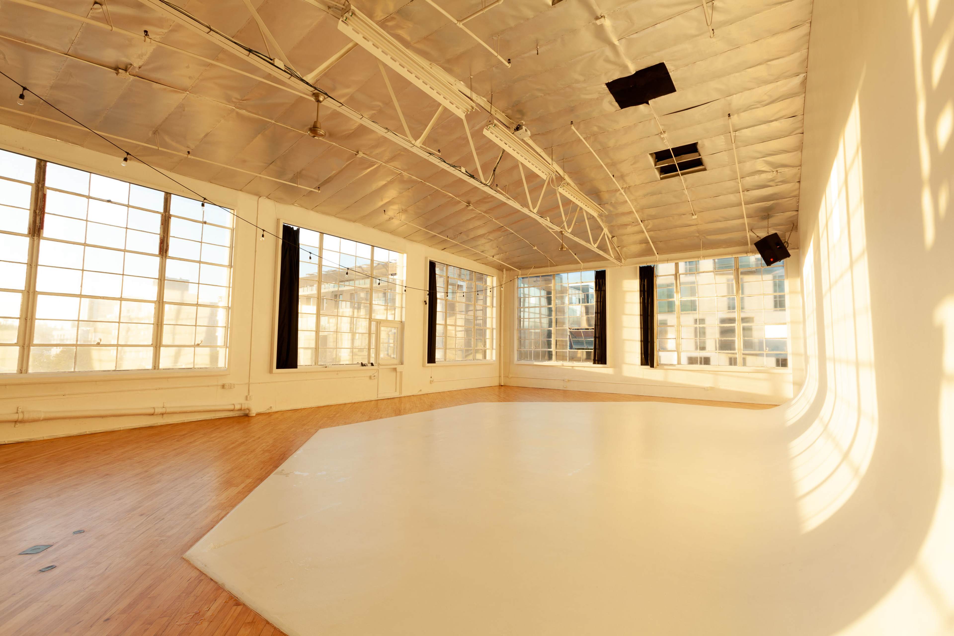 The image shows a spacious, well-lit room with large windows and a smooth, curved wooden floor.