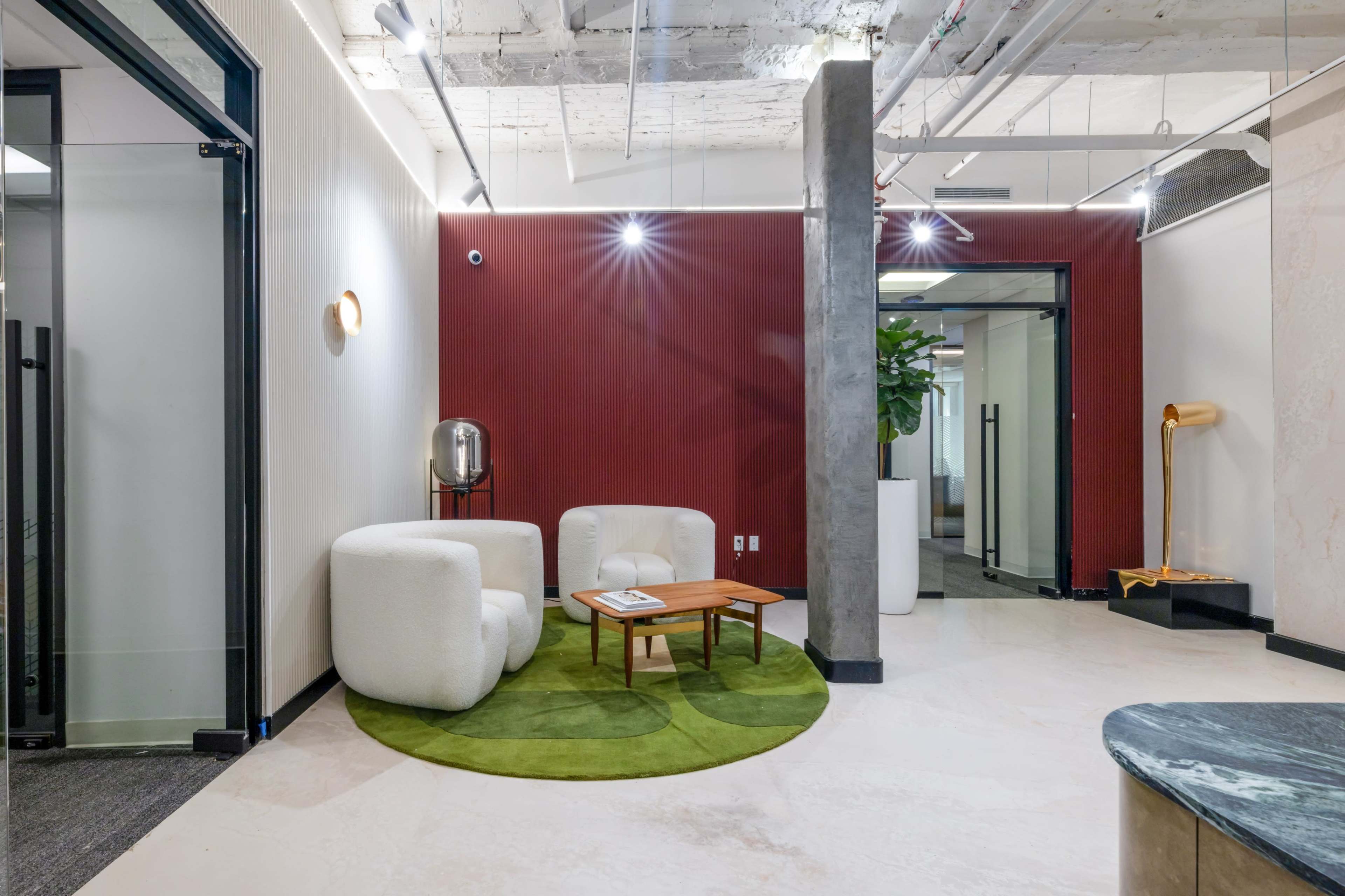 The image displays a modern office interior featuring two white, rounded chairs, a small wooden table, and a green circular rug, complemented by a decorative plant and minimalist lighting.