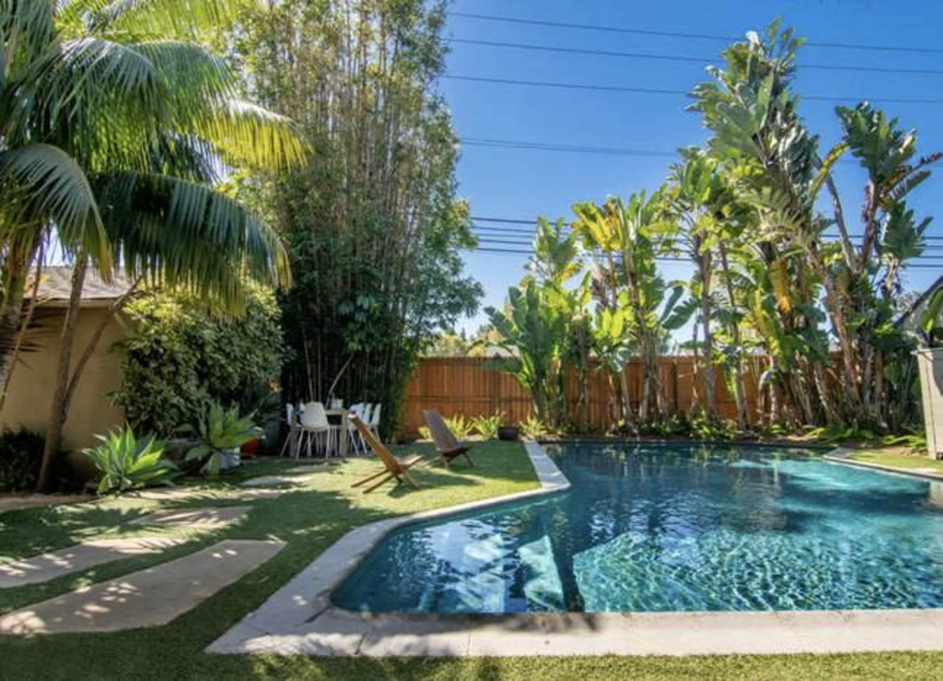 A backyard with a swimming pool surrounded by tropical plants and lounge chairs.