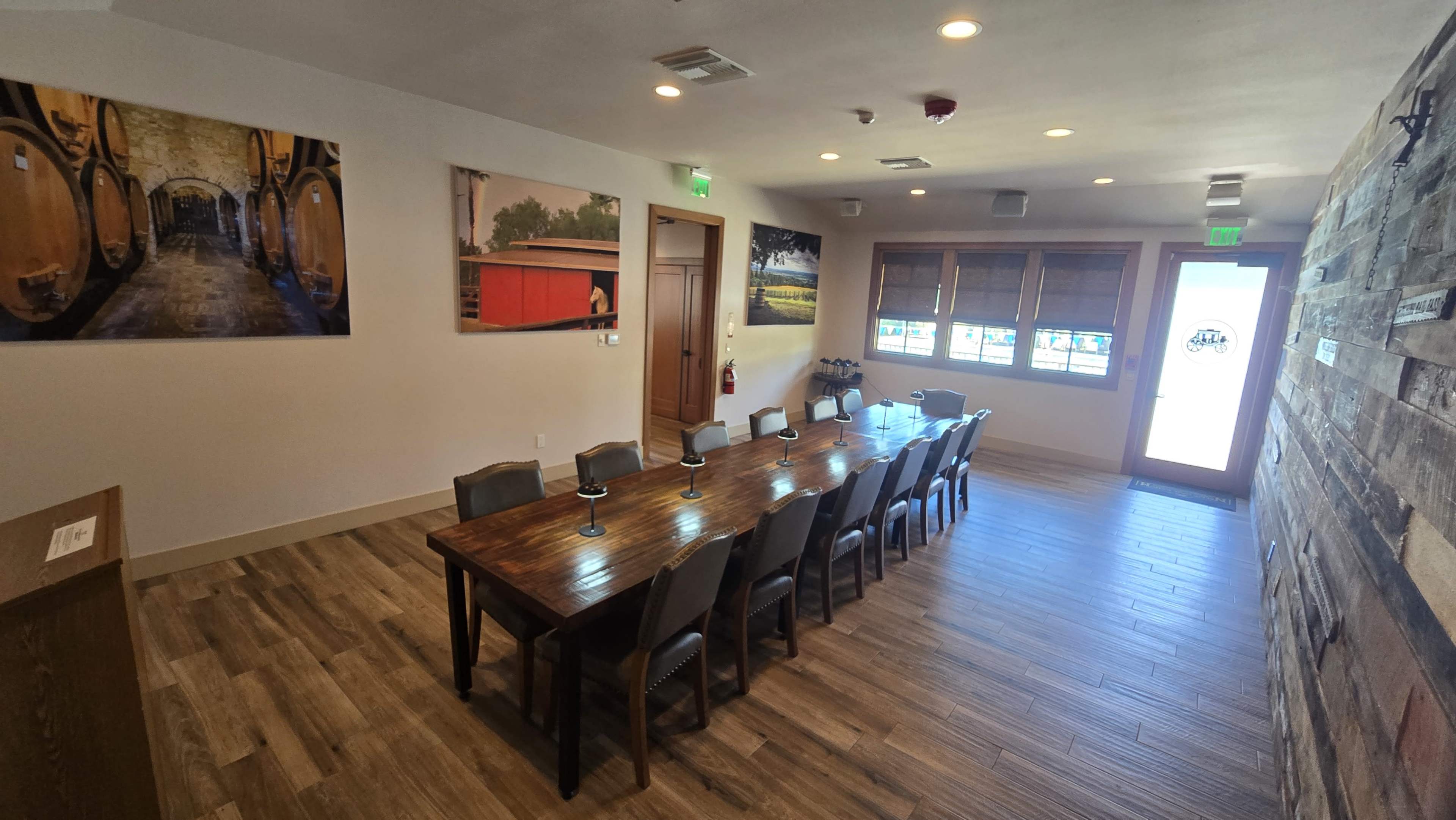 The image shows a spacious meeting room with a long wooden table surrounded by chairs, decorated with photographs on the walls and a large window letting in natural light.
