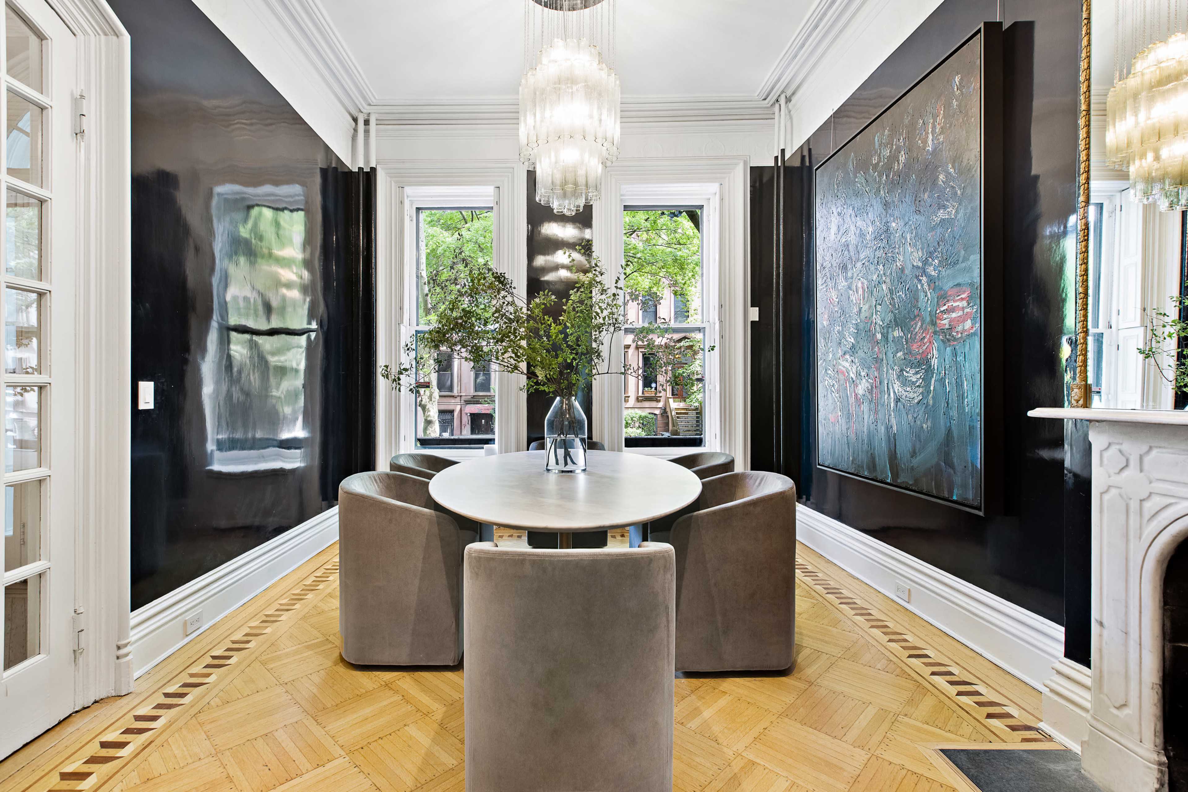 A dining room with a circular table surrounded by upholstered chairs, large windows, and a dark accent wall featuring a piece of artwork.