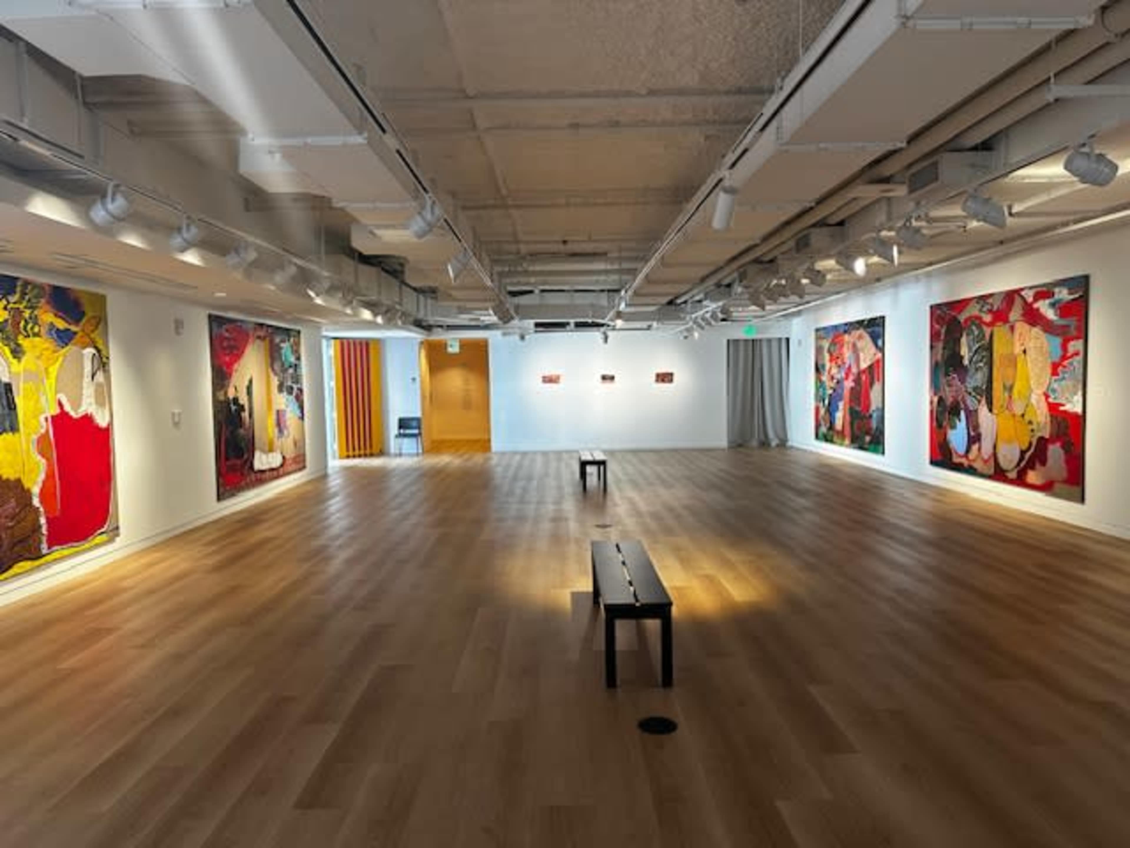 An art gallery featuring large, colorful paintings on the walls and a wooden bench positioned in the center of the room.