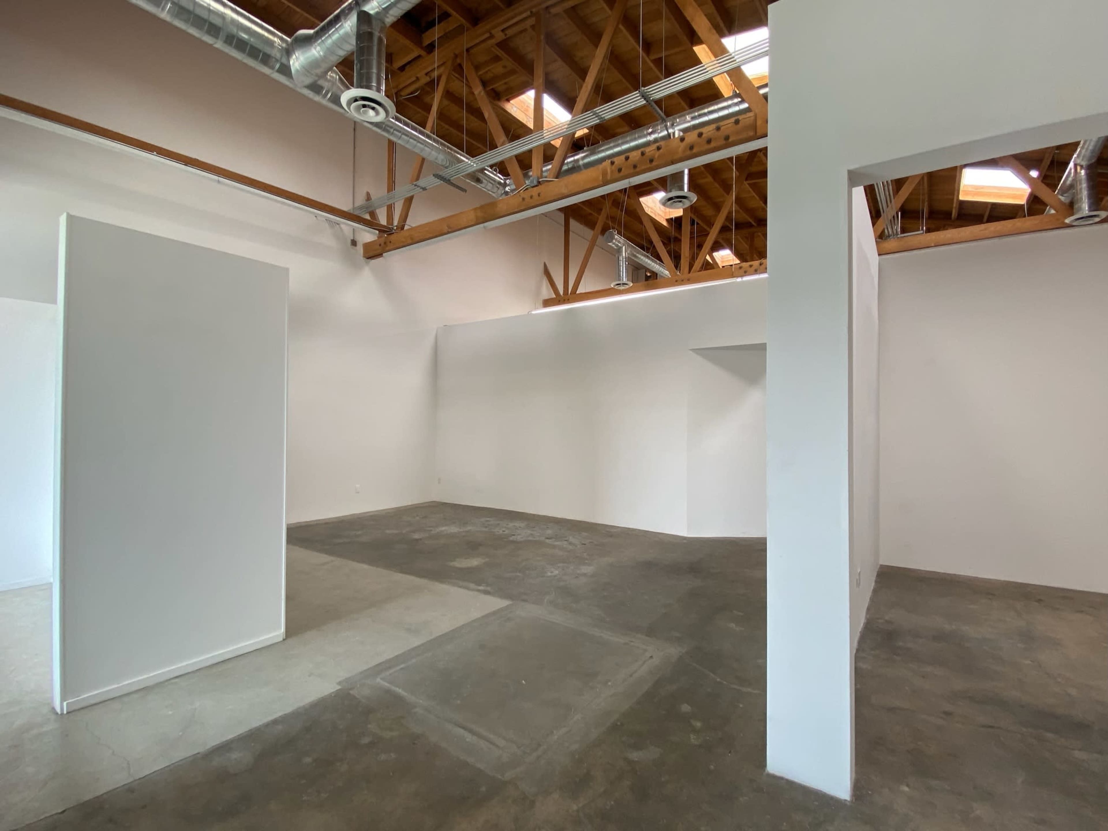 An empty room with white walls, exposed wooden beams, and concrete flooring.