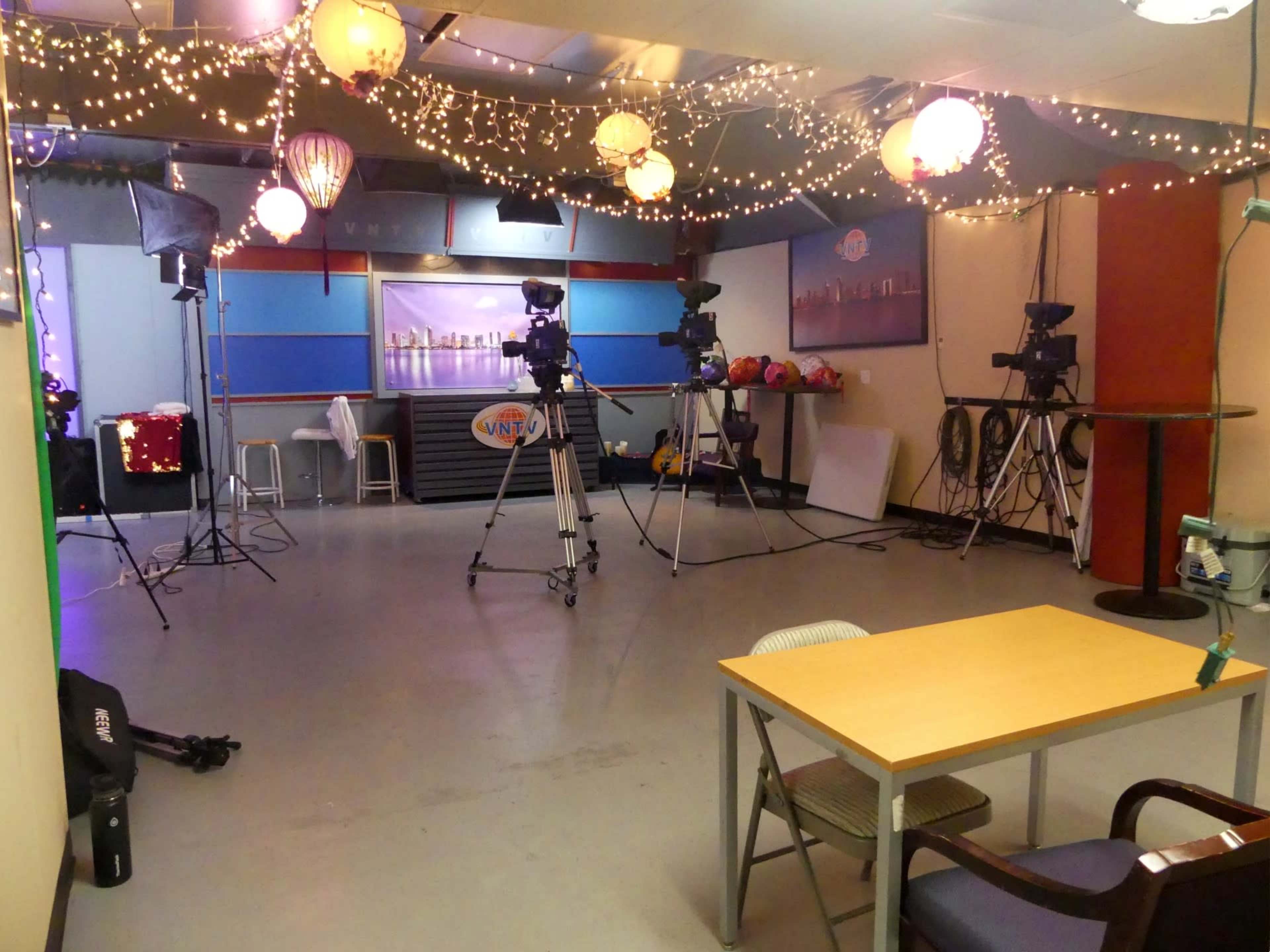 A brightly lit studio space with cameras, a table, and decorative lights hanging from the ceiling.