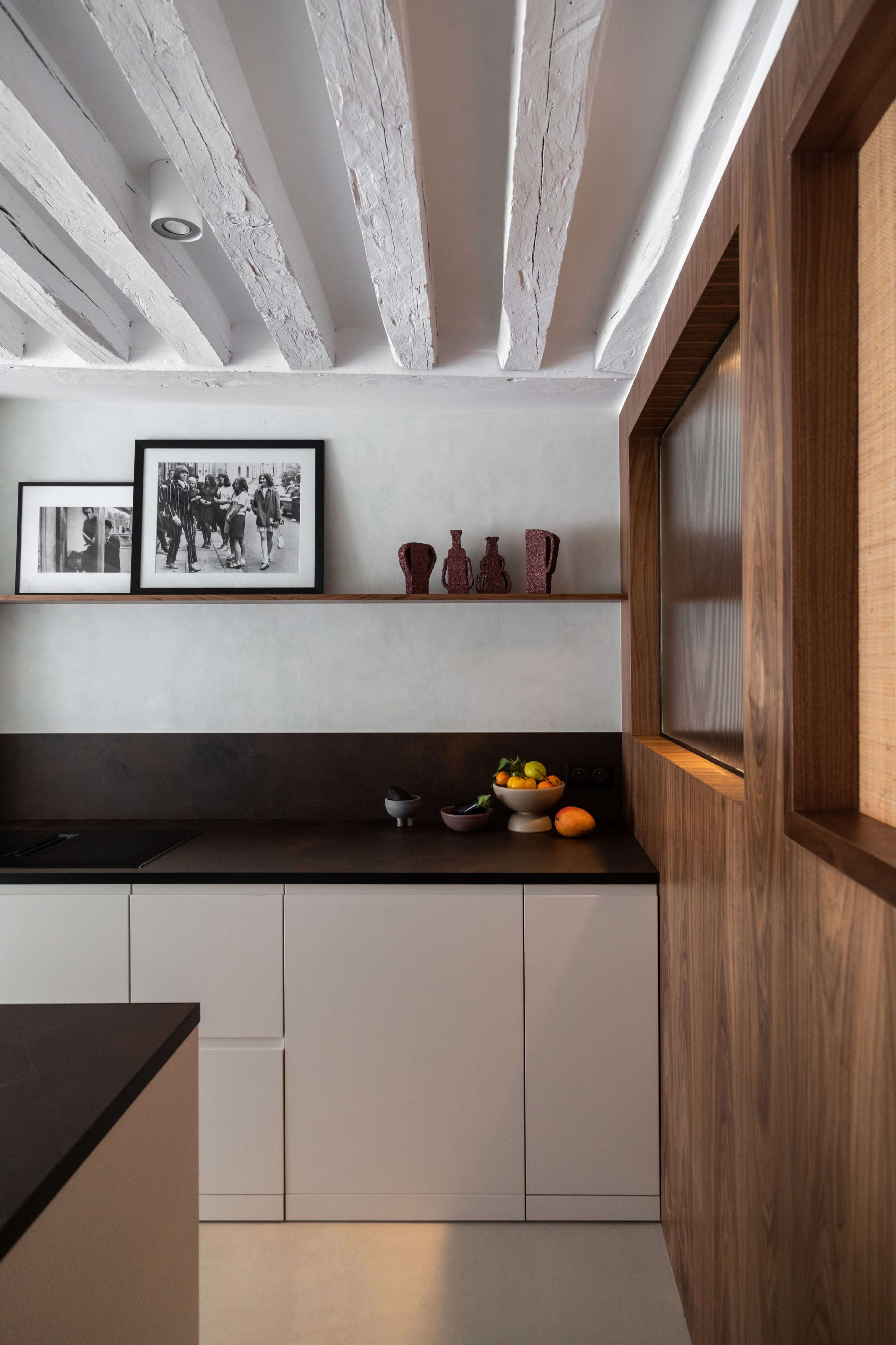 A modern kitchen features a white color scheme, wooden accents, open shelving with decorative items, and a bowl of fruit on the countertop.