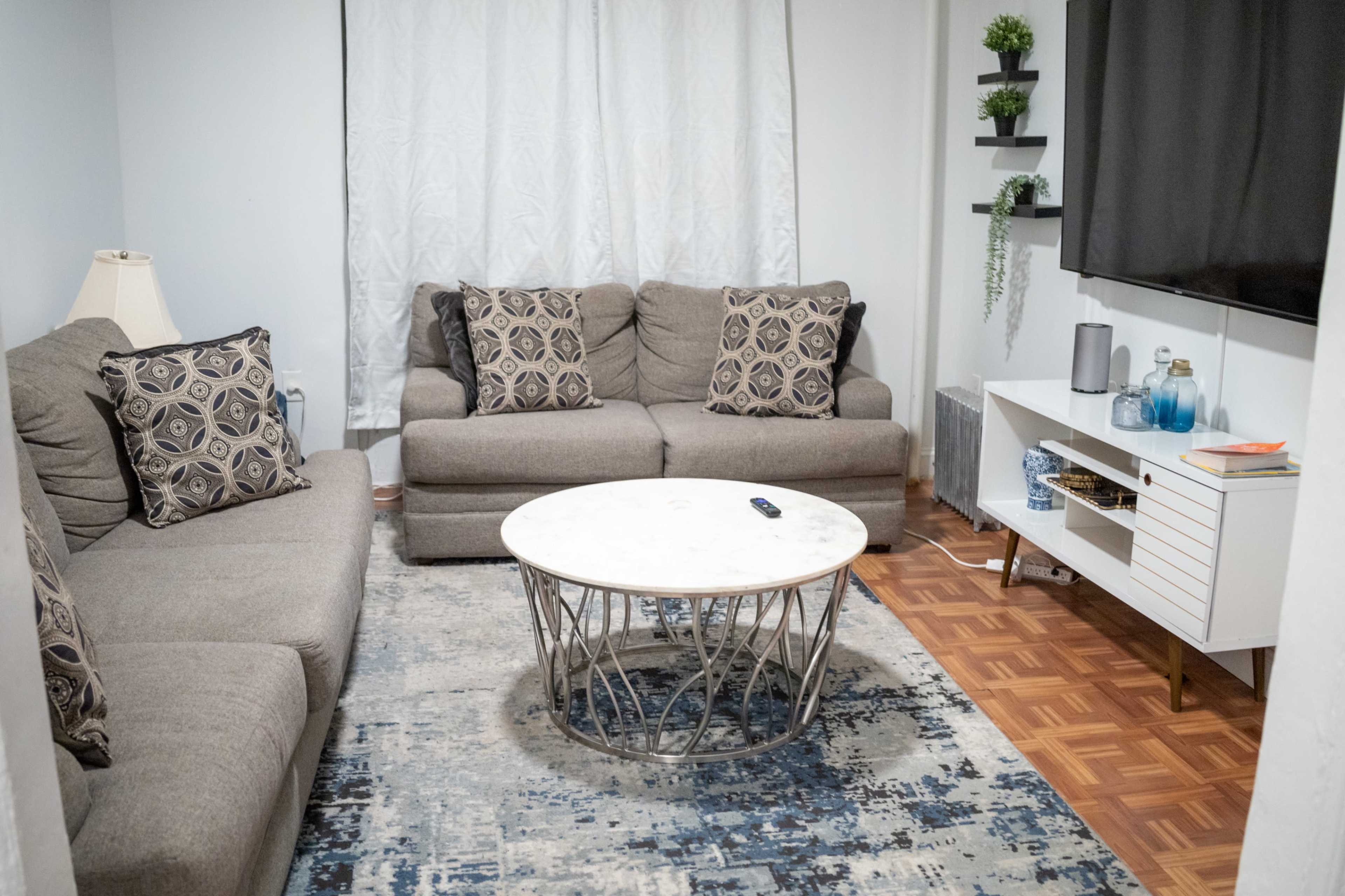 A living room with two gray sofas, a round marble coffee table, and a television mounted on the wall, with a rug covering the floor.