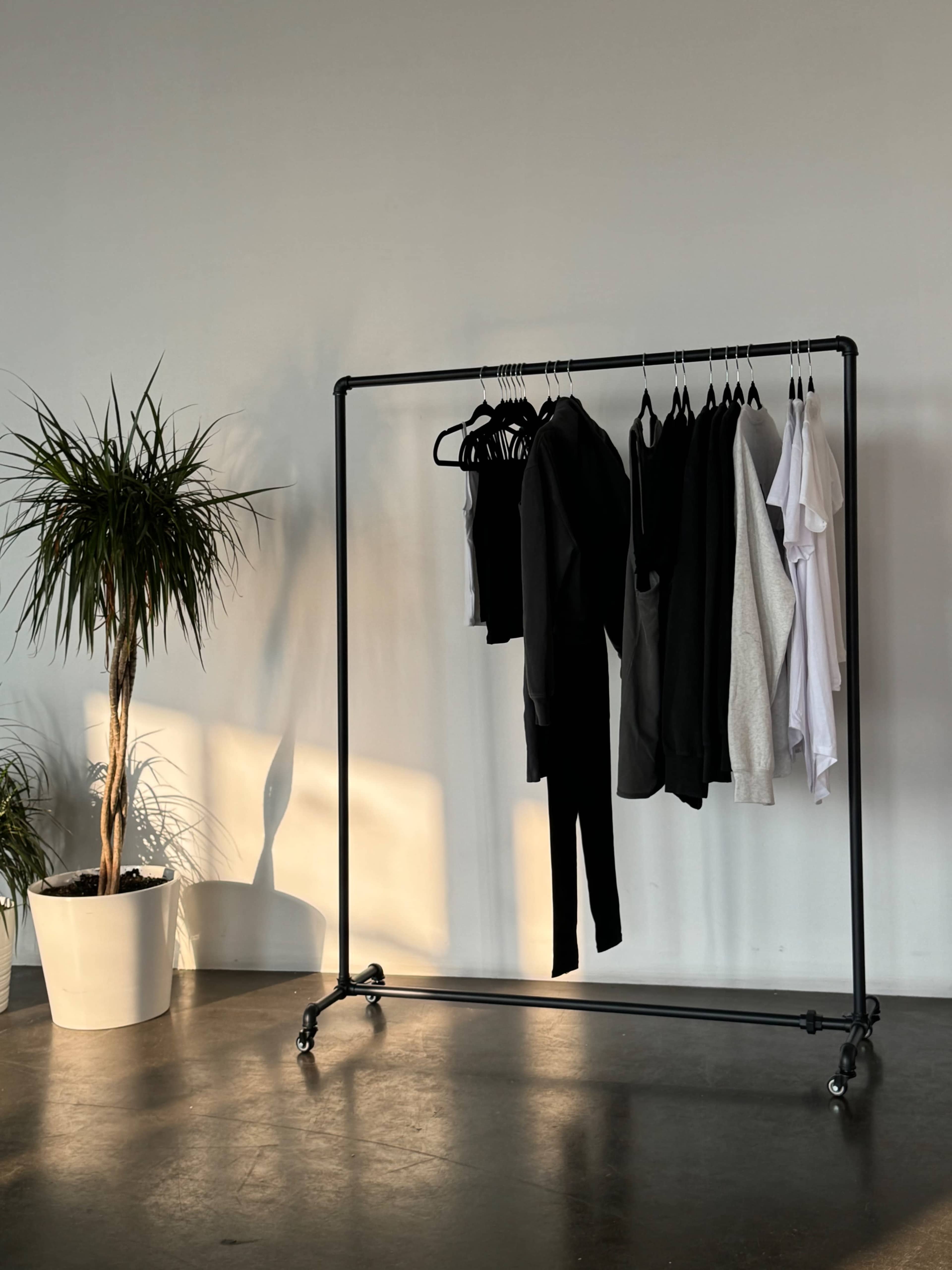 A clothing rack with a variety of garments hangs beside a potted plant in a minimalist interior space.