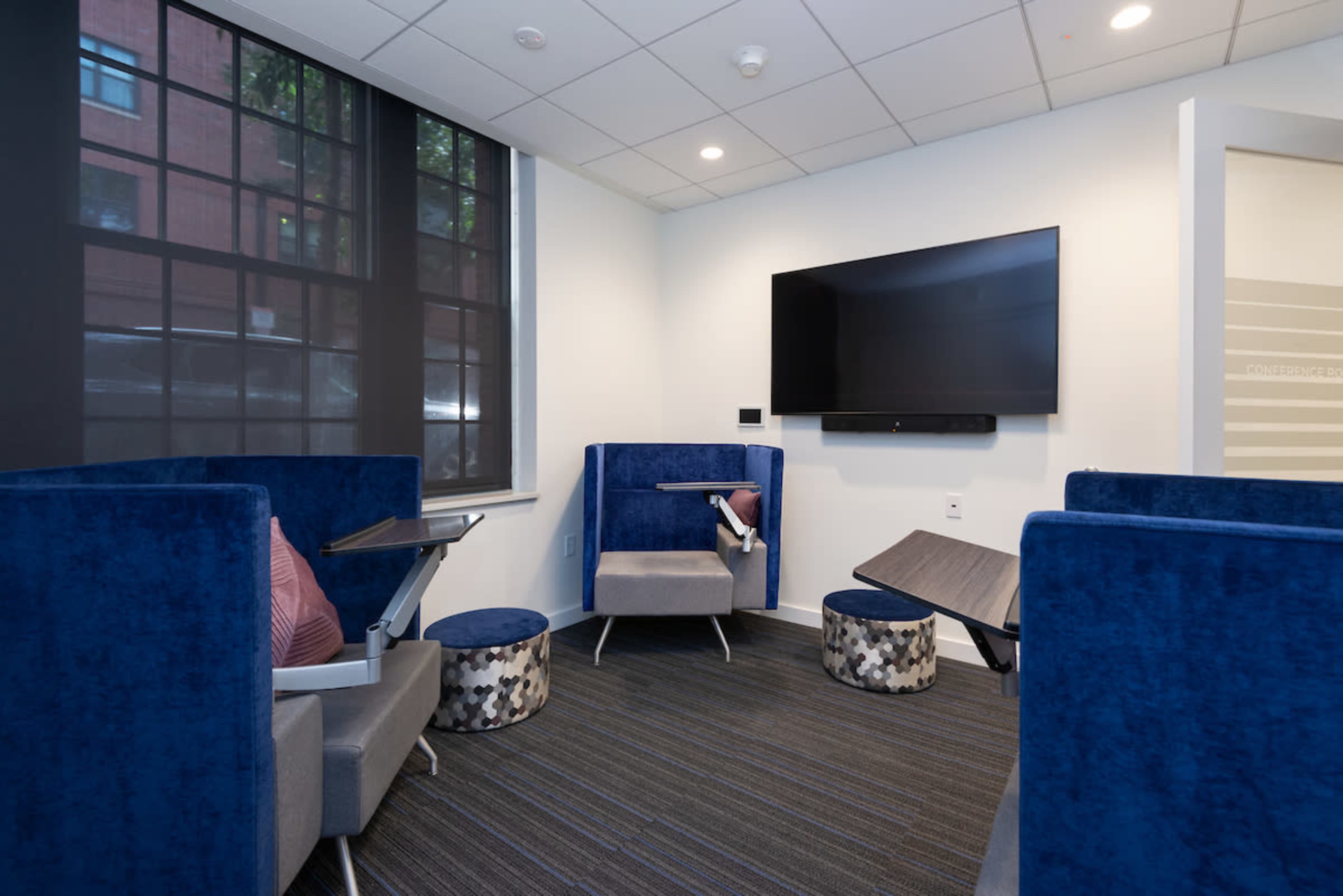 A small lounge area with blue upholstered seating, small tables, and a wall-mounted television.