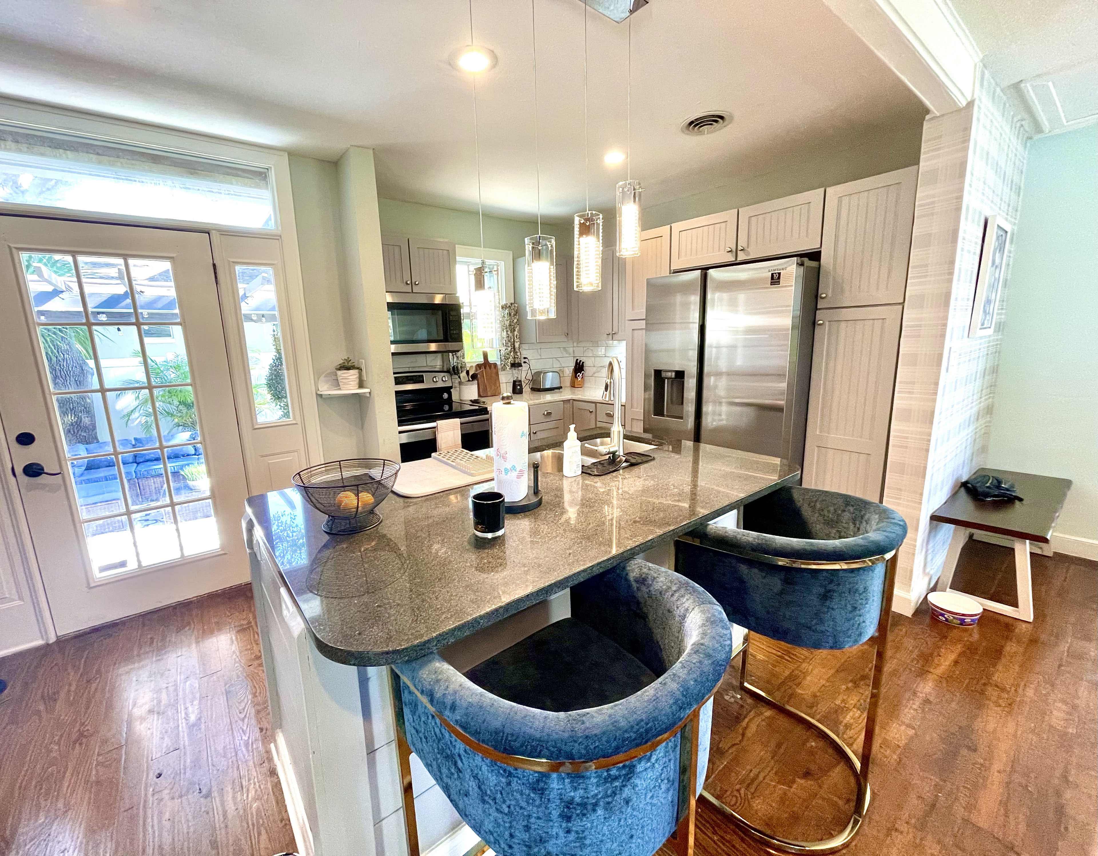 A modern kitchen features a central island with bar stools, stainless steel appliances, and a door leading to an outdoor space.
