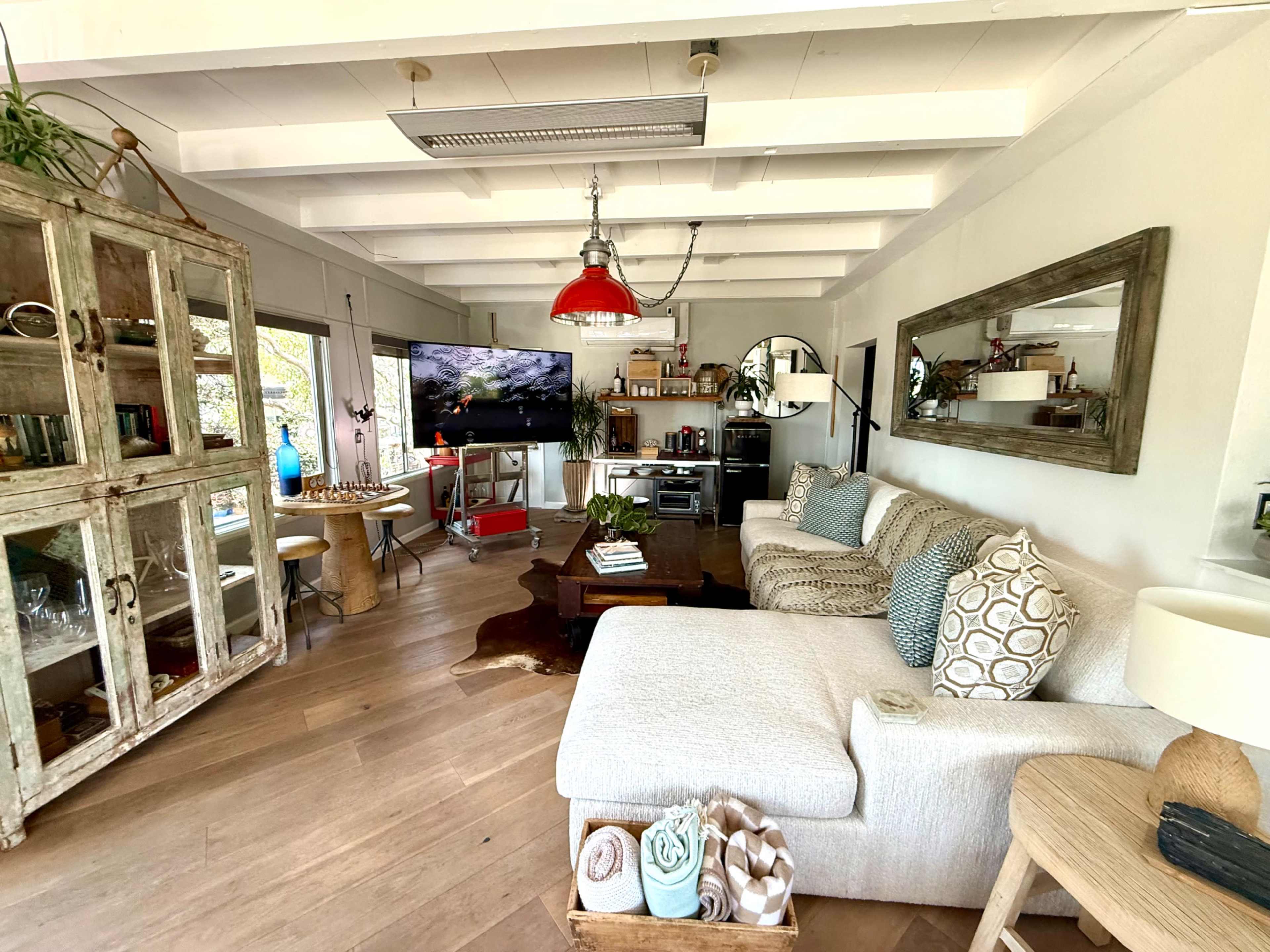 The image shows a cozy living room featuring a large sectional sofa, a television mounted on the wall, and a mix of decorative furniture and plants.