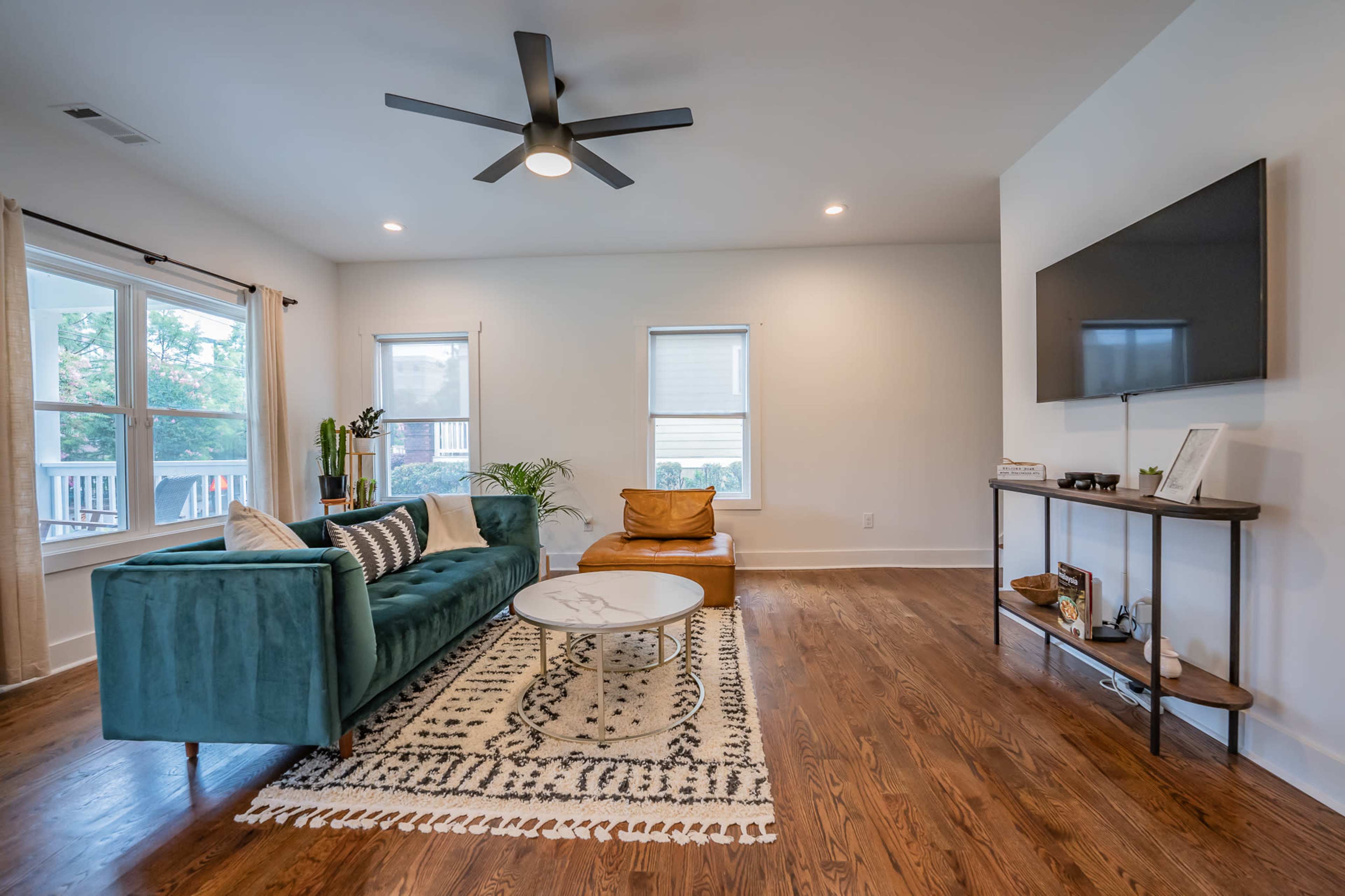 A modern living room featuring a teal sofa, a circular coffee table, and a flat-screen TV mounted on the wall.