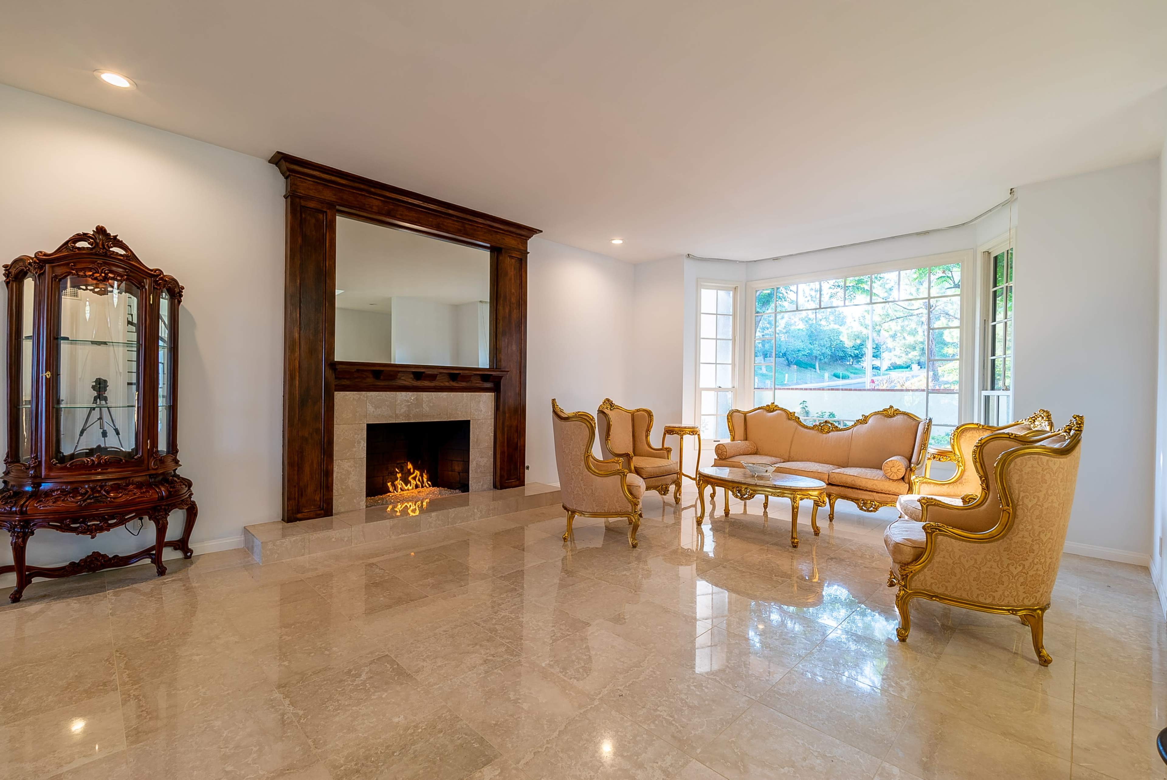 A bright living room with marble flooring, a decorative fireplace, and elegant gold-accented furniture arranged around a central coffee table.