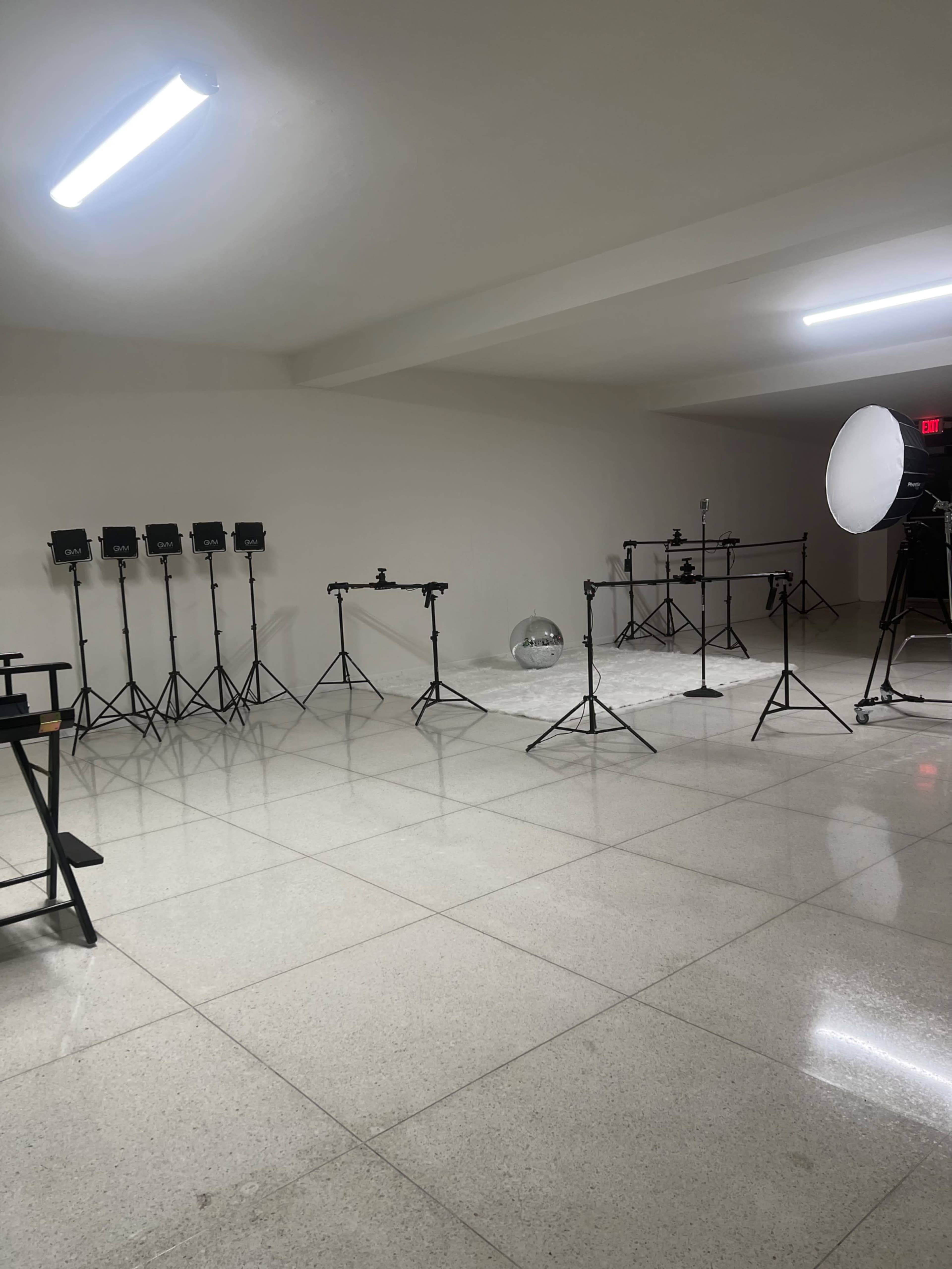 A photography studio setup with various lighting equipment, stands, and a large reflector in a spacious room.