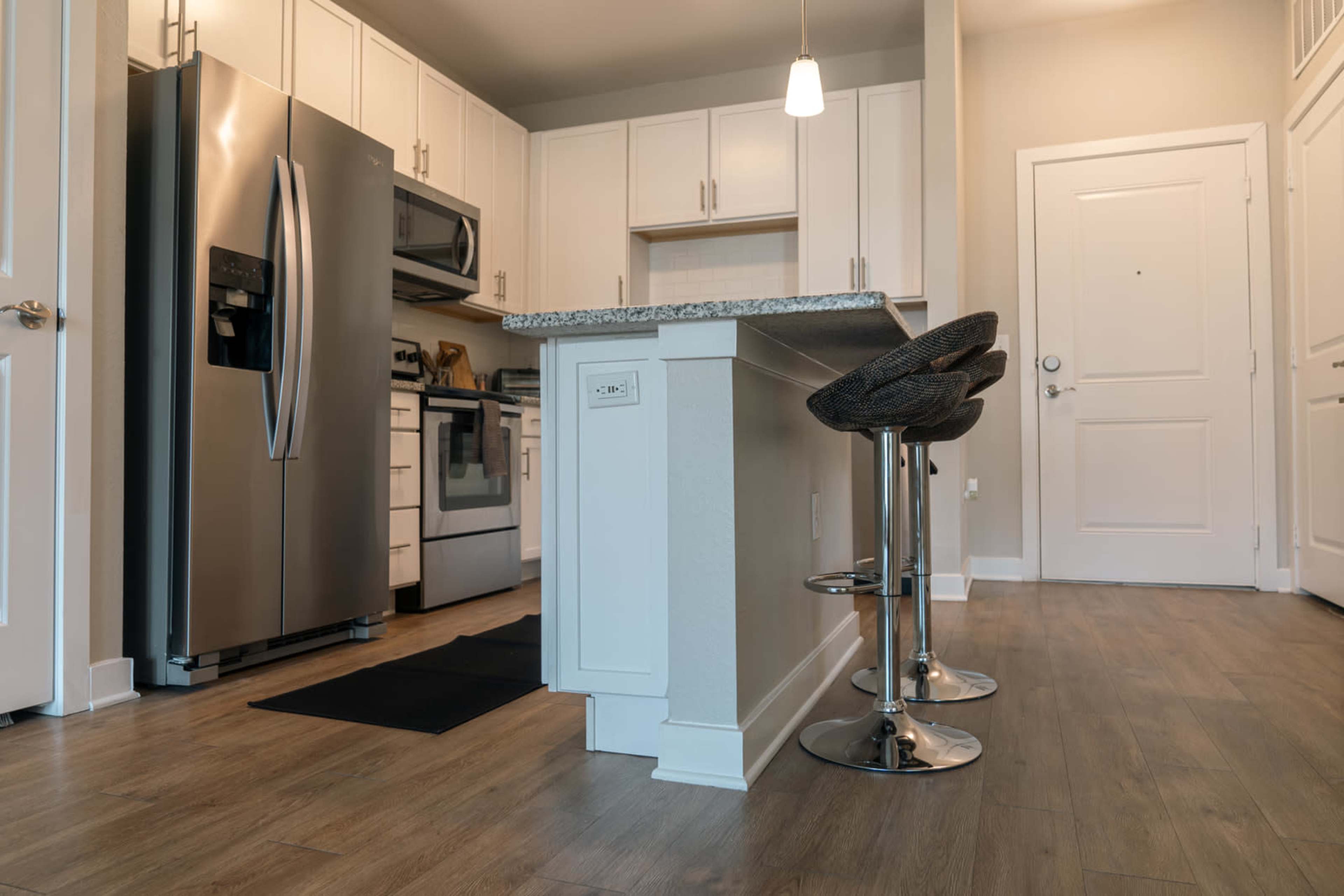 A modern kitchen with stainless steel appliances, white cabinetry, and a countertop with two bar stools.