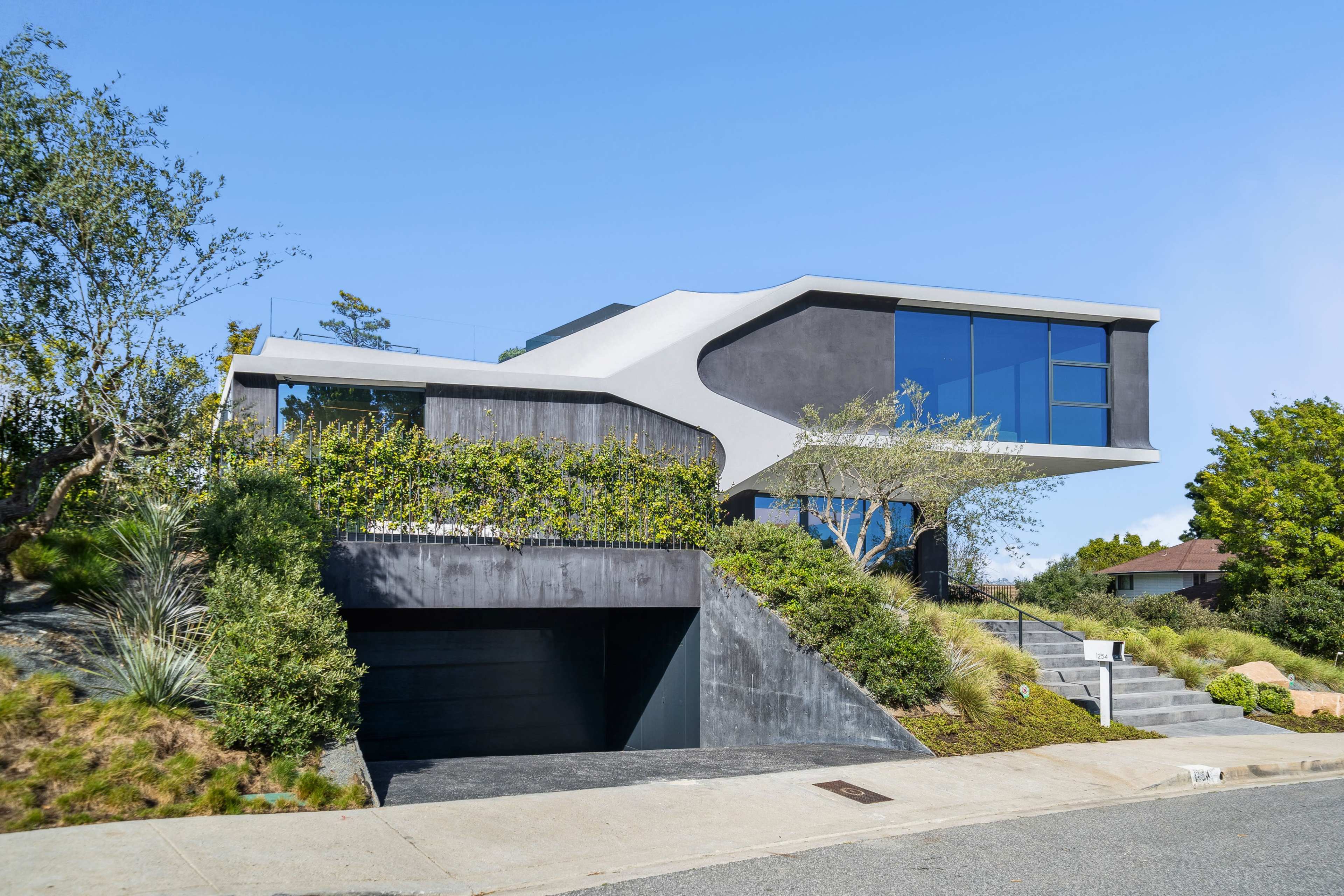 A modern two-story house features a distinctive angular design with large windows and a landscaped front yard.