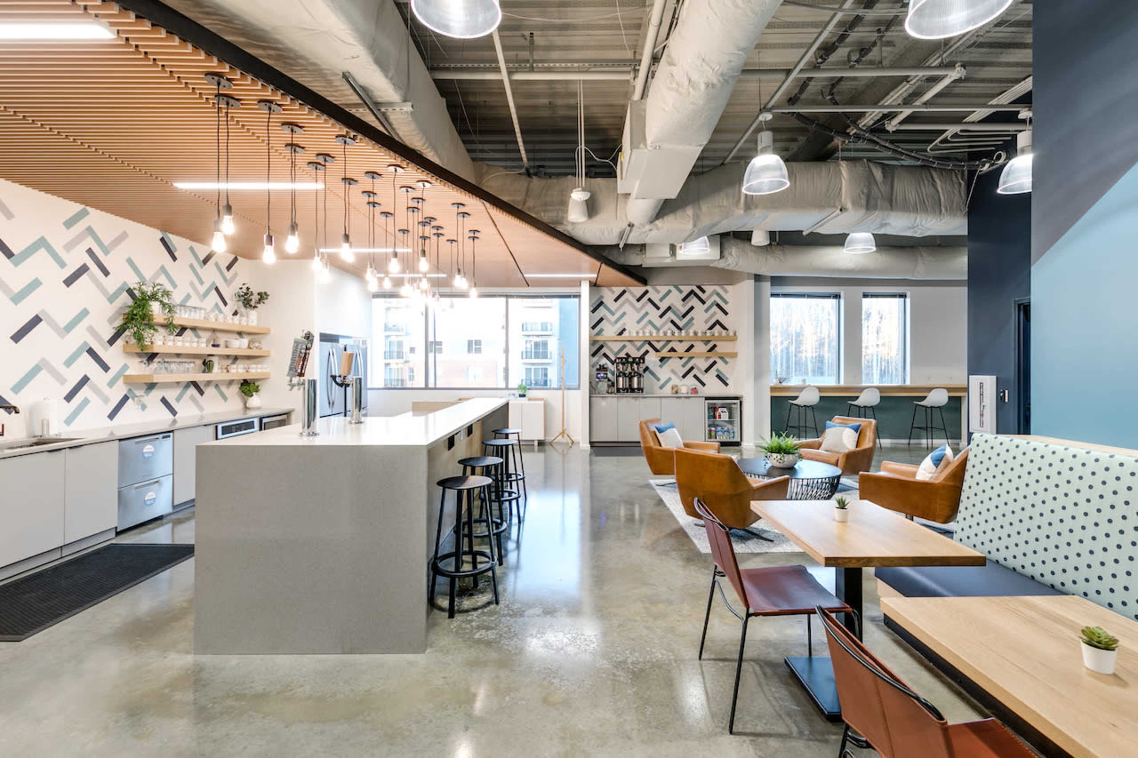 A modern kitchen area with a large island, bar stools, and various seating arrangements, surrounded by geometric wall decorations and large windows.