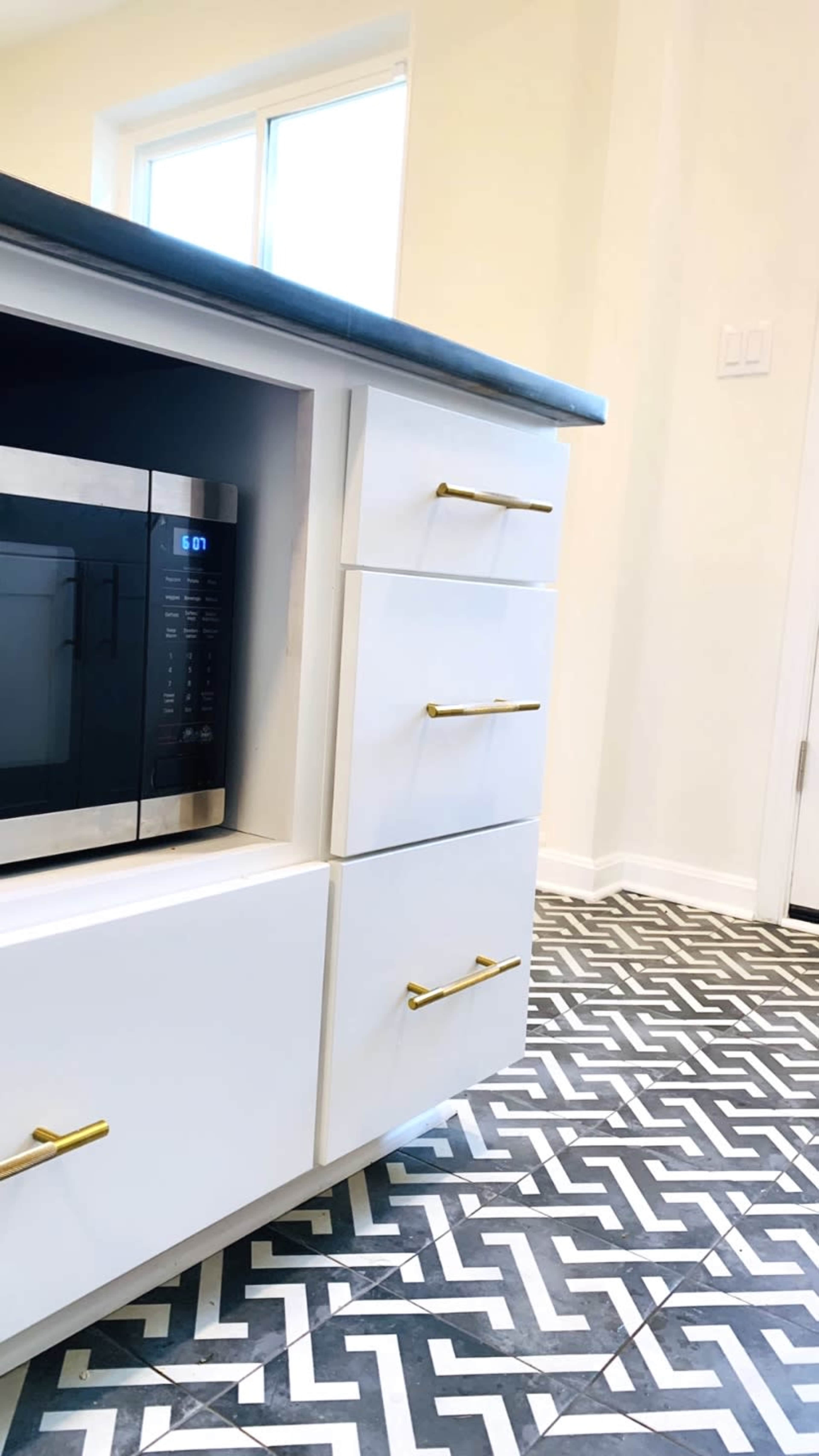 A kitchen corner with a white cabinet, a microwave inside, and patterned black and white flooring.