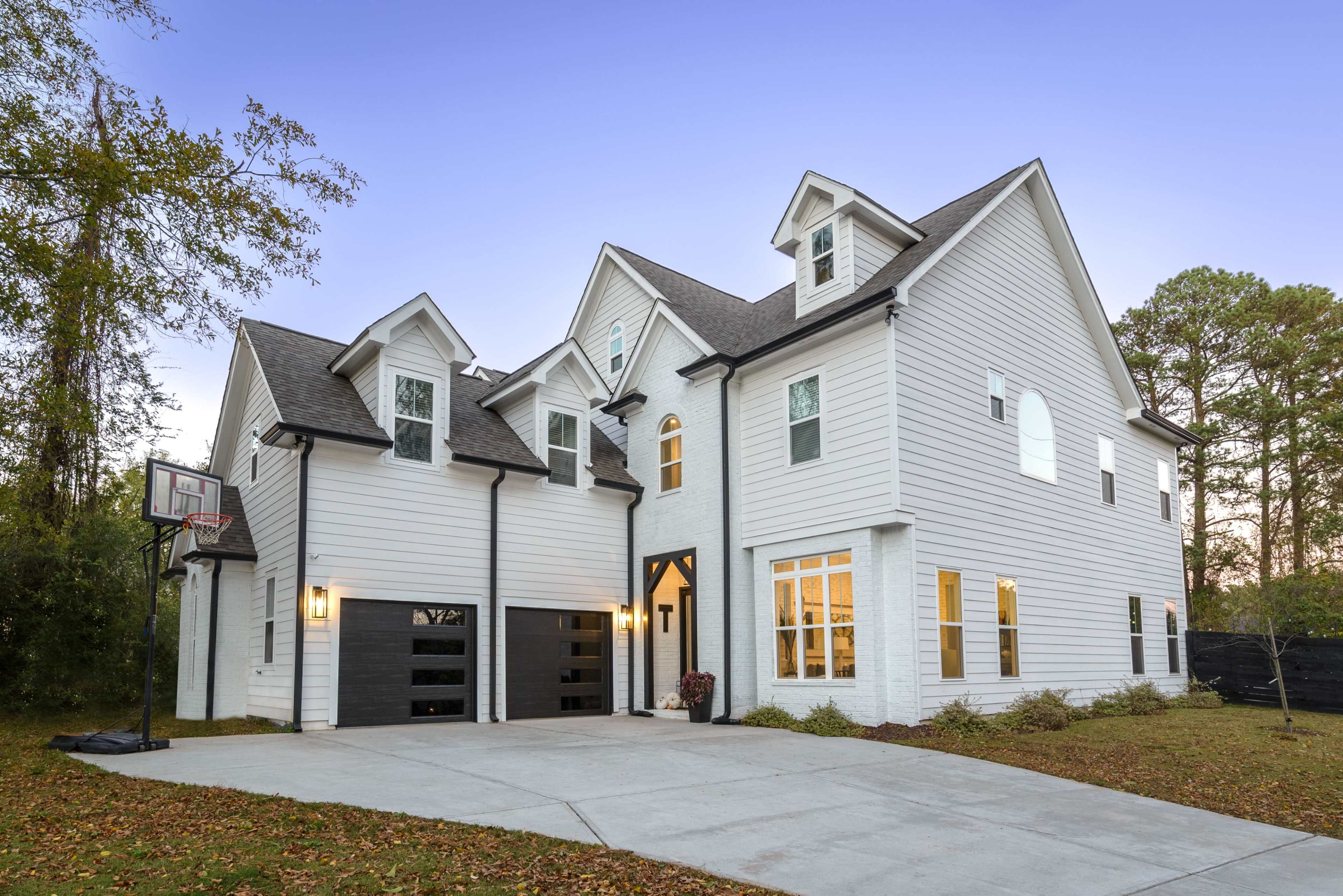 The image shows a modern two-story white house with black accents and a basketball hoop in the driveway.