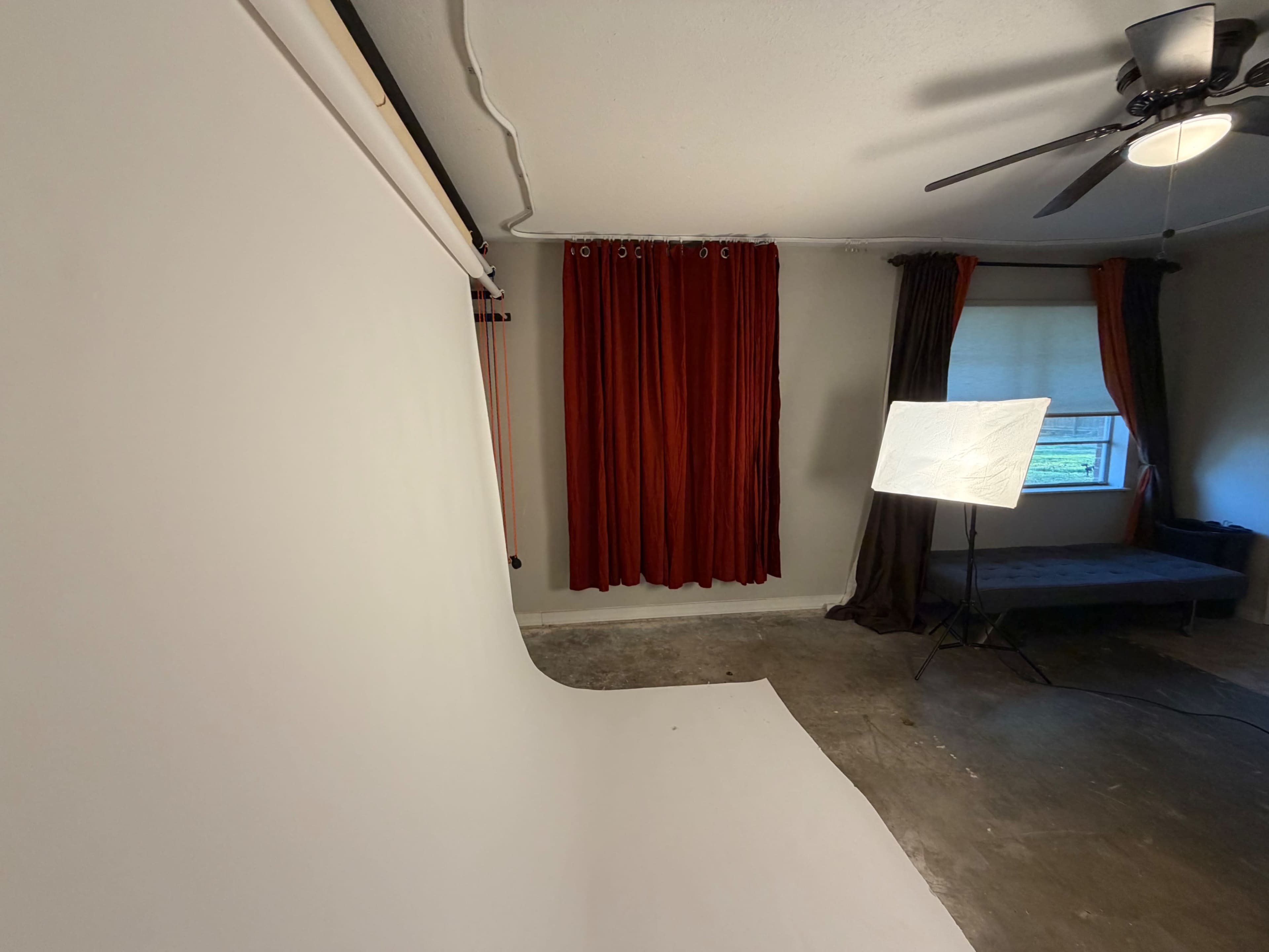 The image shows a photography studio with a white backdrop, red curtains, and a softbox light set up in a partially furnished room.