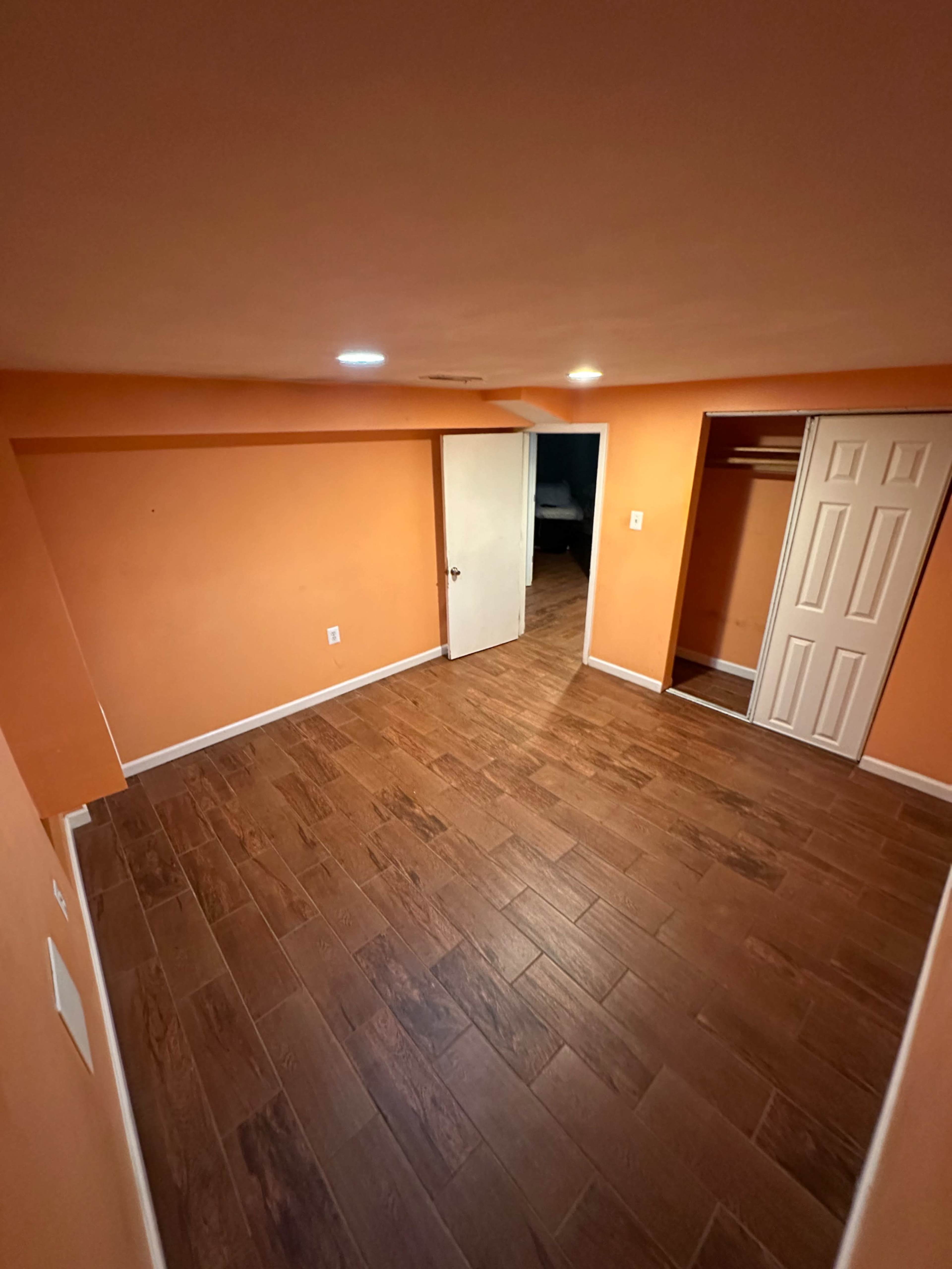 The image shows a small, empty room with orange walls, a wooden floor, and a door leading to a closet.