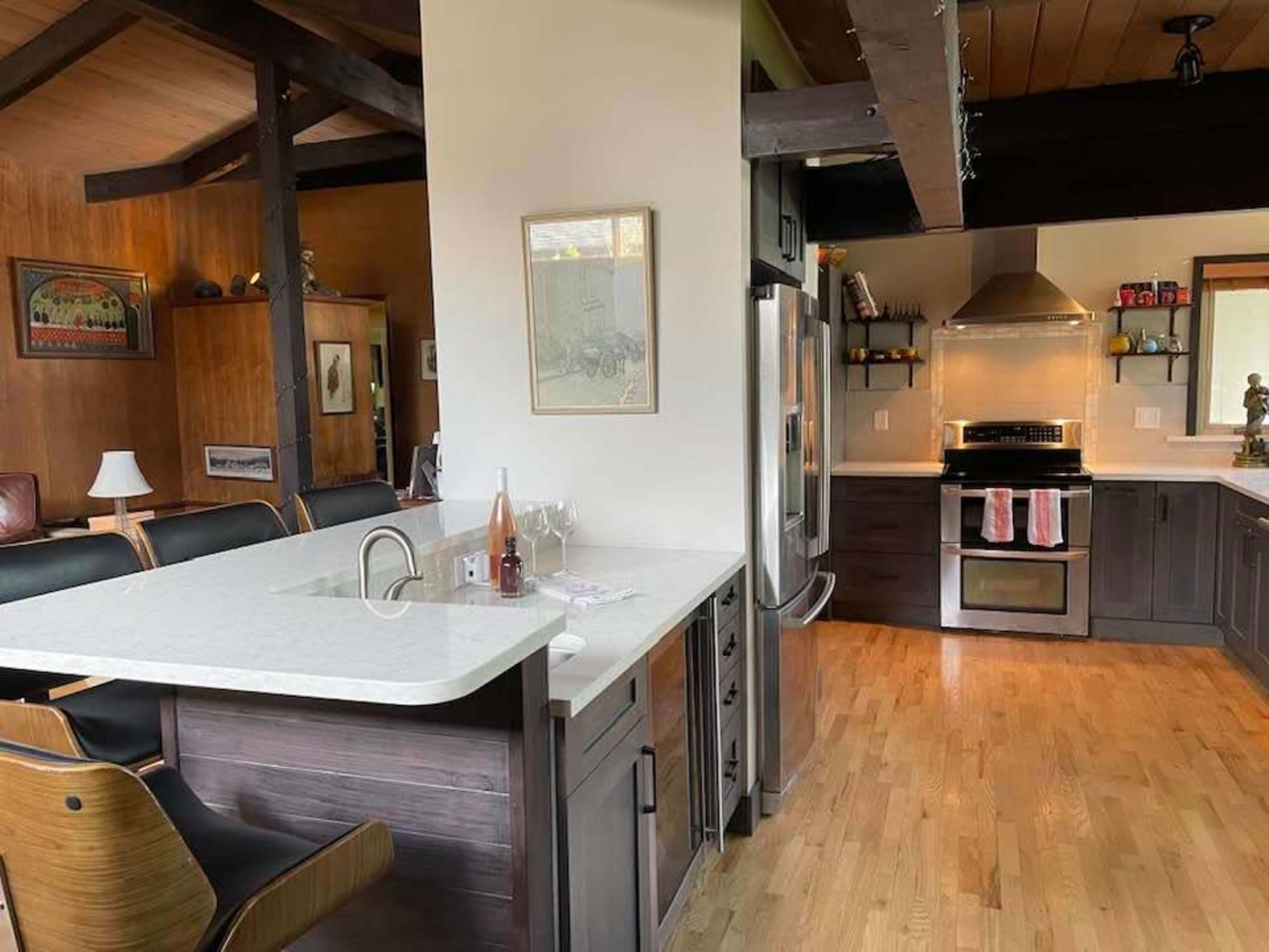 A modern kitchen with a large island featuring a sink and bar seating, open to a dining area with wooden beams and a contemporary layout.