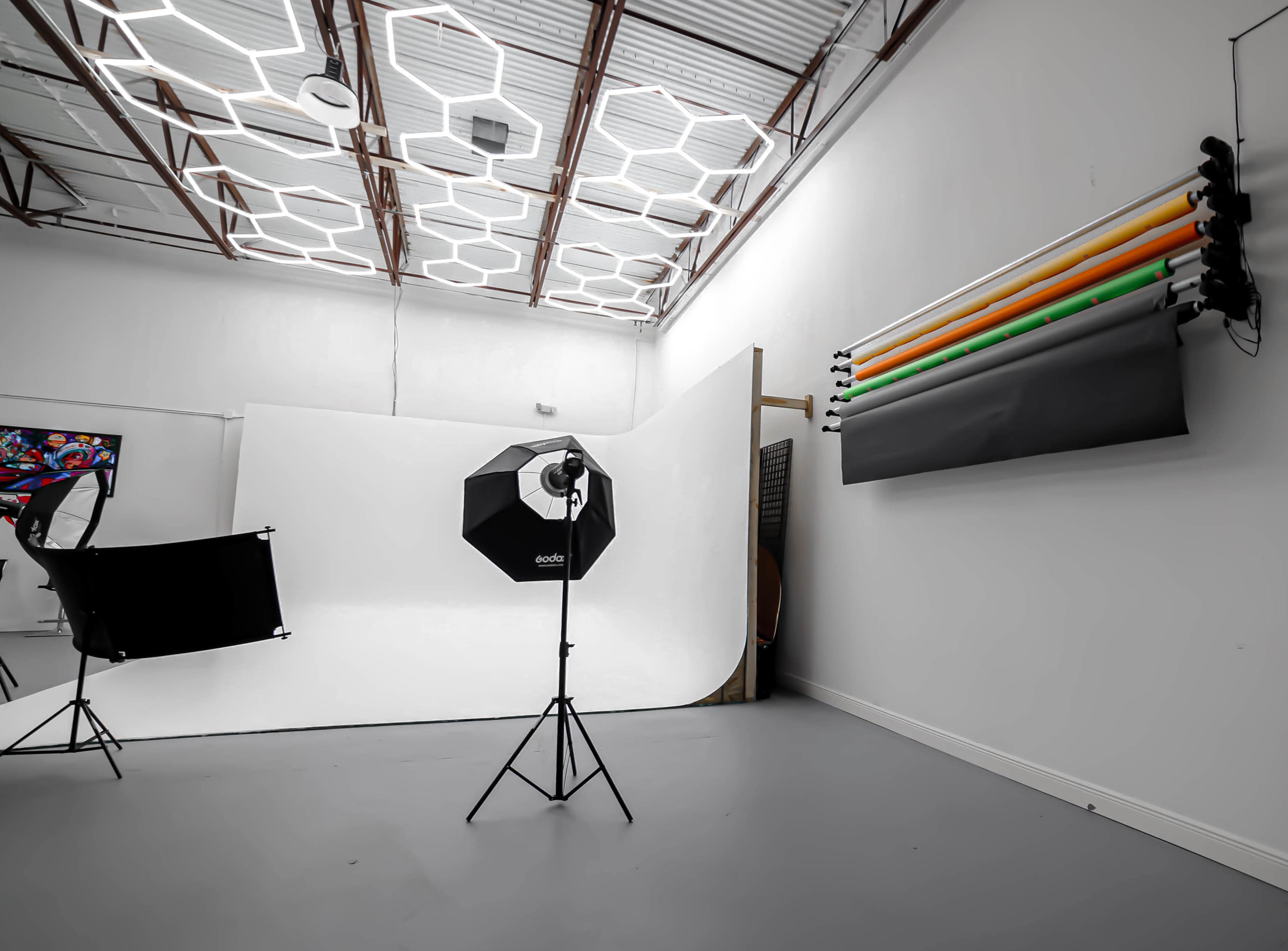 A photography studio with a white backdrop, lighting equipment, and color backdrops hanging on the wall.