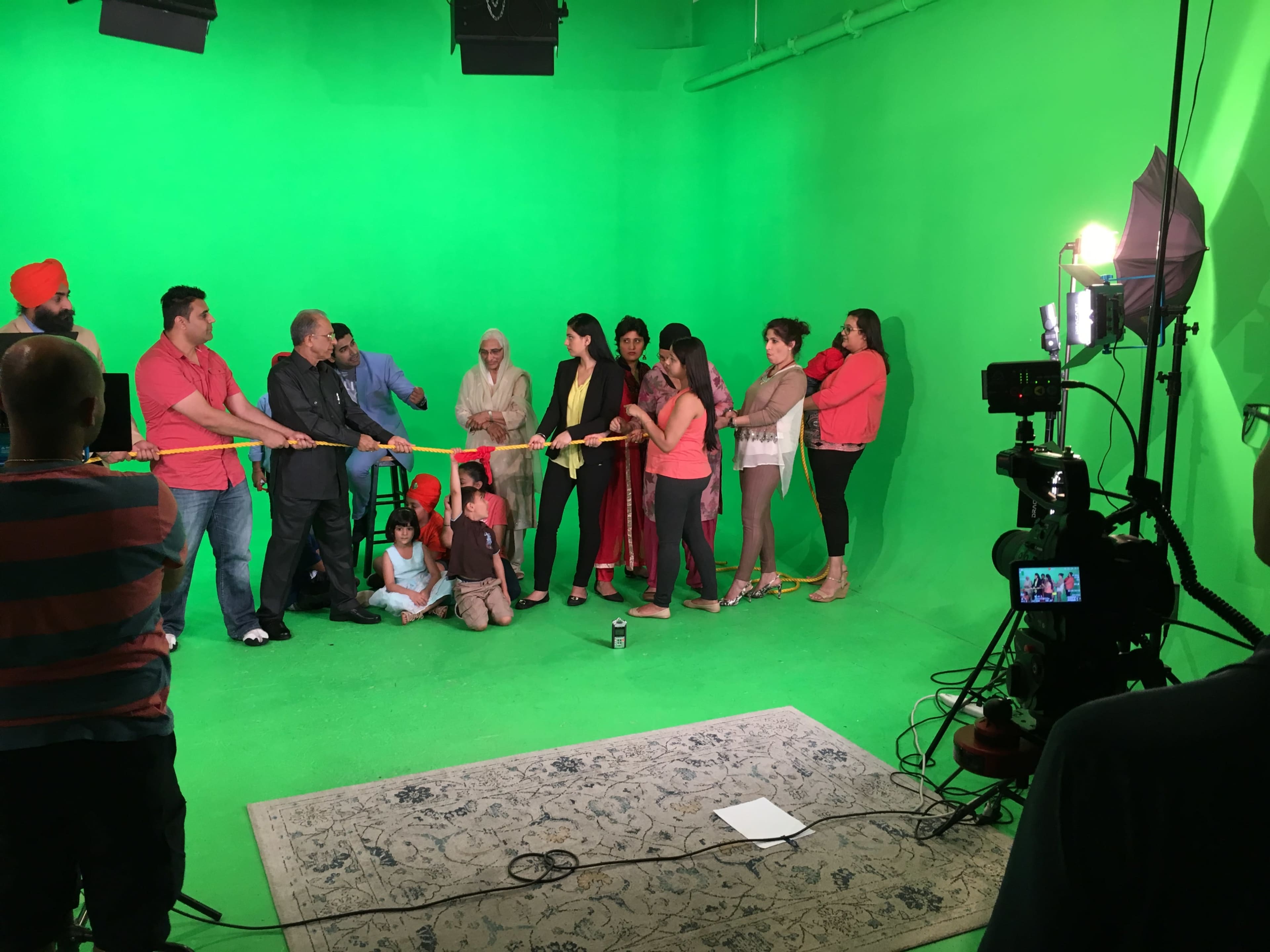 A group of people stands in a green screen studio, participating in a ribbon-cutting ceremony while a camera setup captures the scene.